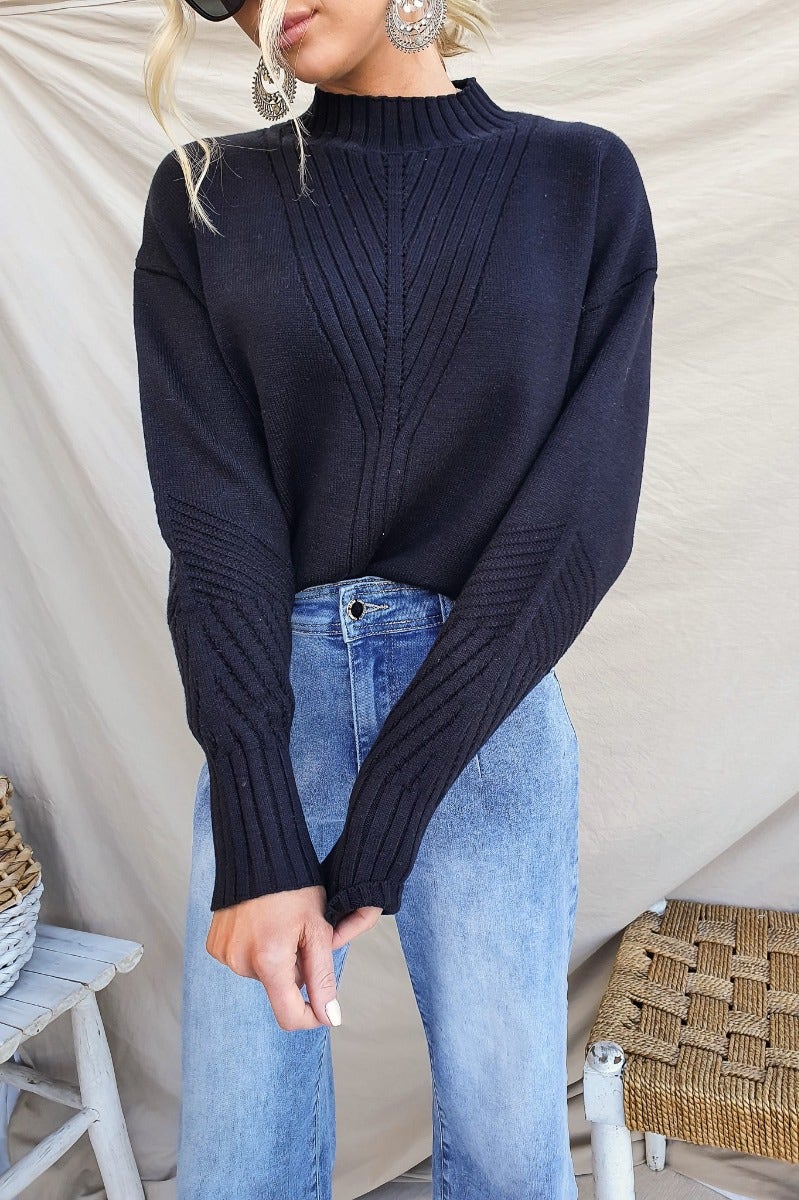 Black ribbed knit Cuba jumper with a mock neckline and relaxed fit, styled with high-waisted jeans.