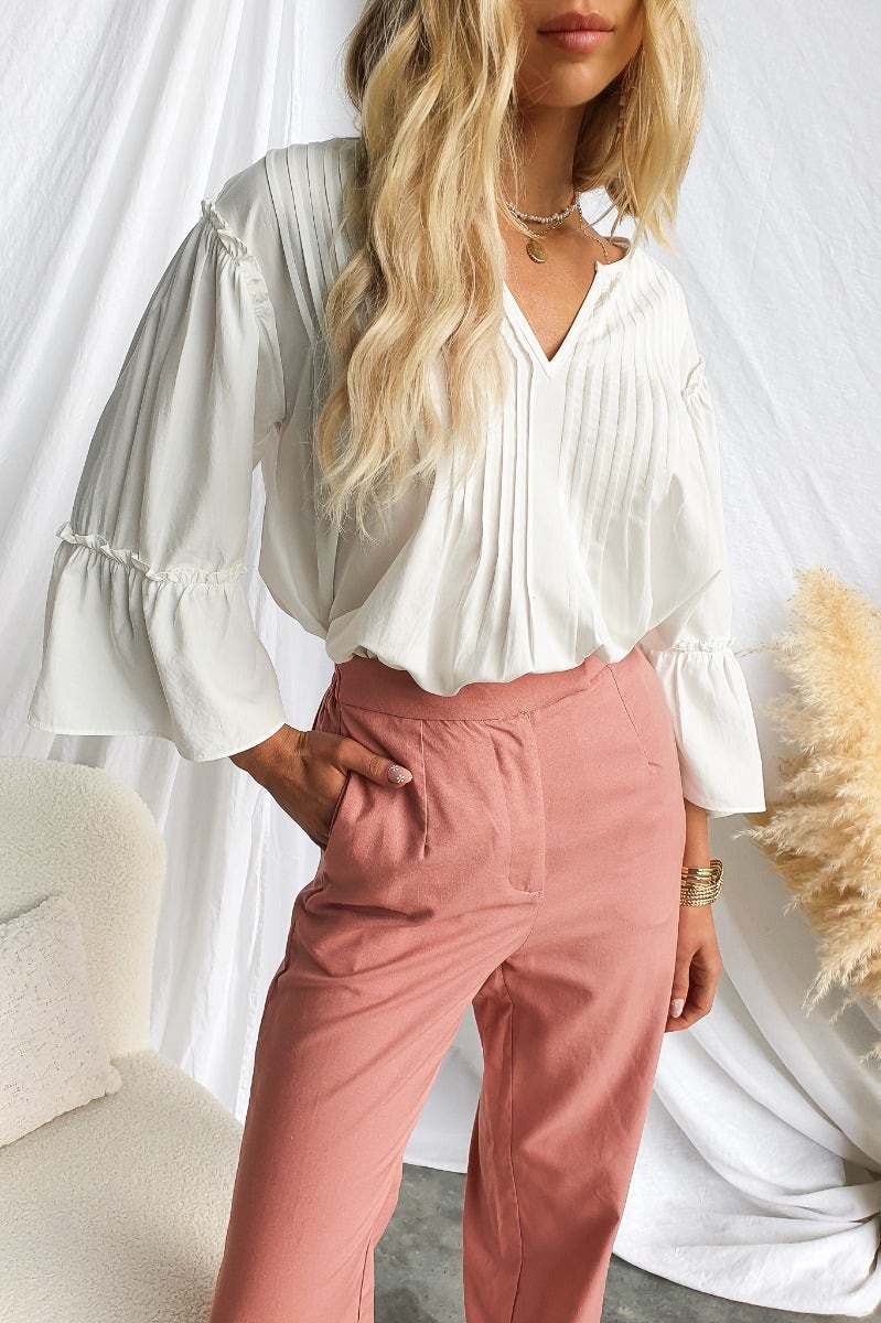 Model wearing a relaxed-fit Cove Top in white cotton blend with pleat detail, paired with pink trousers.