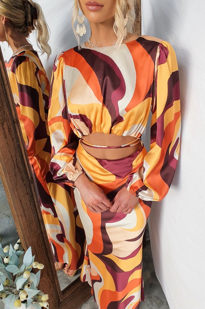 Model wearing a colorful Goldie Maxi Dress with a cut-out waist and flowing sleeves, featuring bold patterns and a tie detail.