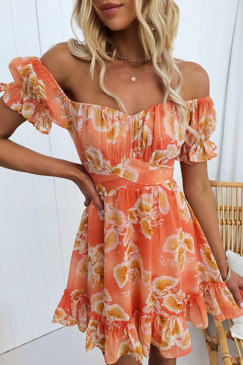 Model wearing a golden sunset floral print dress with elastic sleeves and ruffled hem, ideal for summer outings.