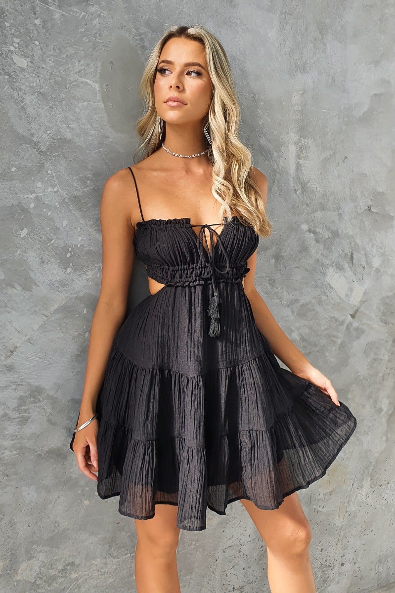 Model wearing a black Spirited Dress with adjustable straps and tie detail, showcasing a stylish summer look.