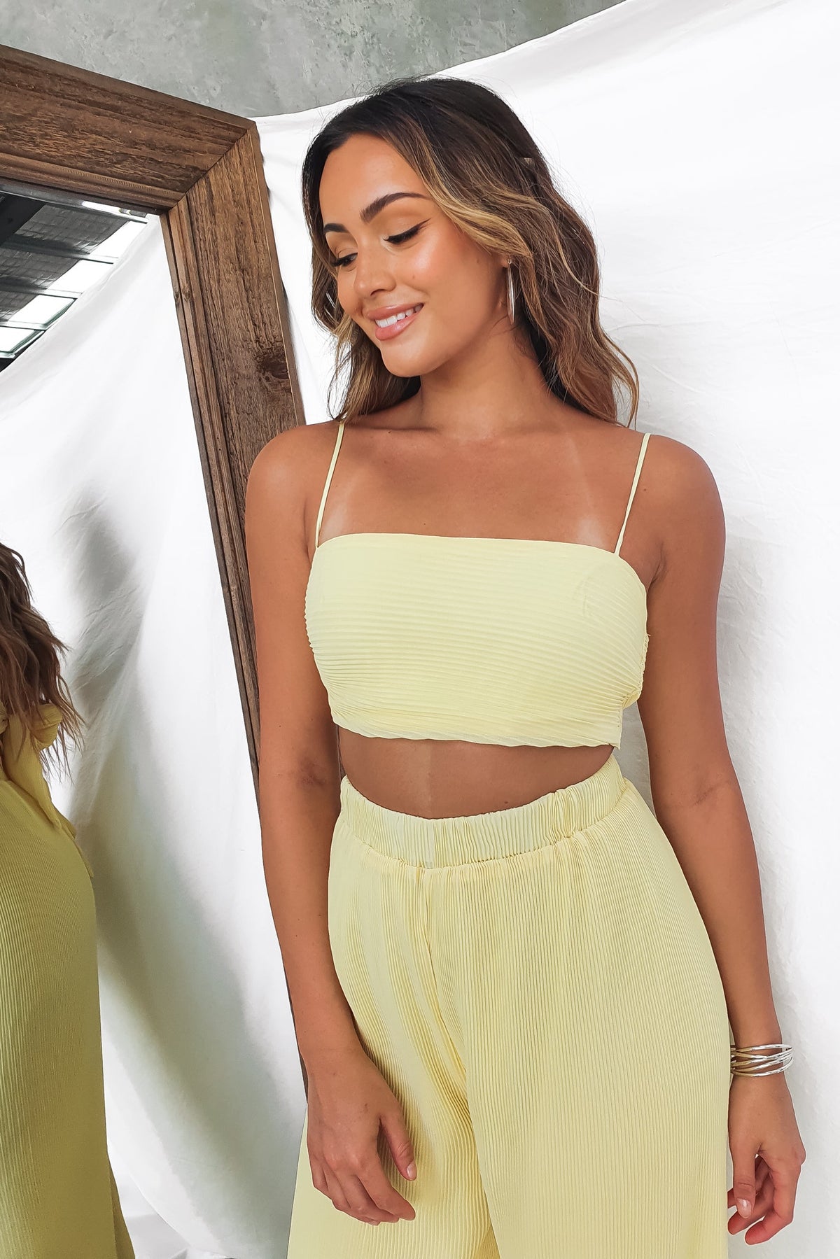 Model wearing the Elida Top in soft yellow, featuring adjustable straps and a stylish pleated design.