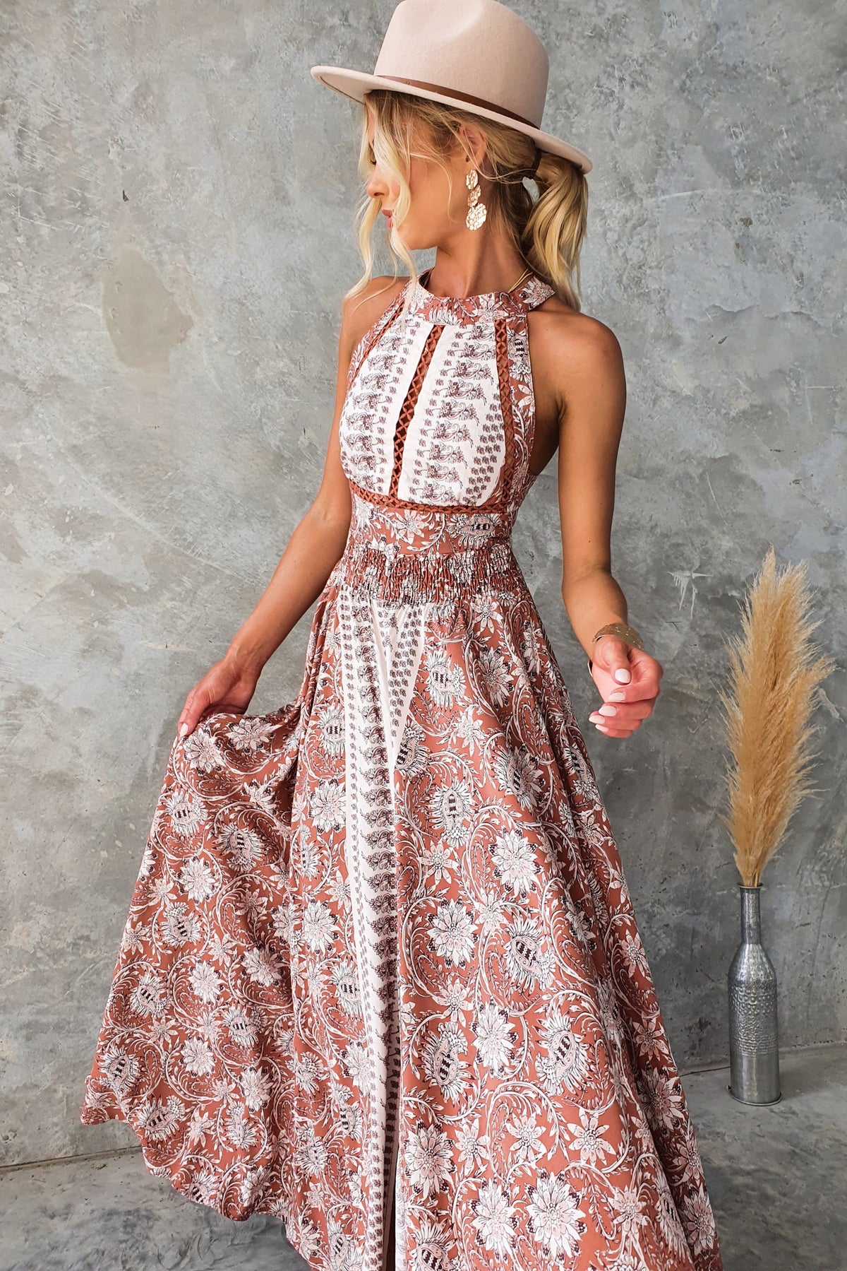 Relly Maxi Dress featuring abstract print, halter neckline, and a front split, styled with a beige hat.