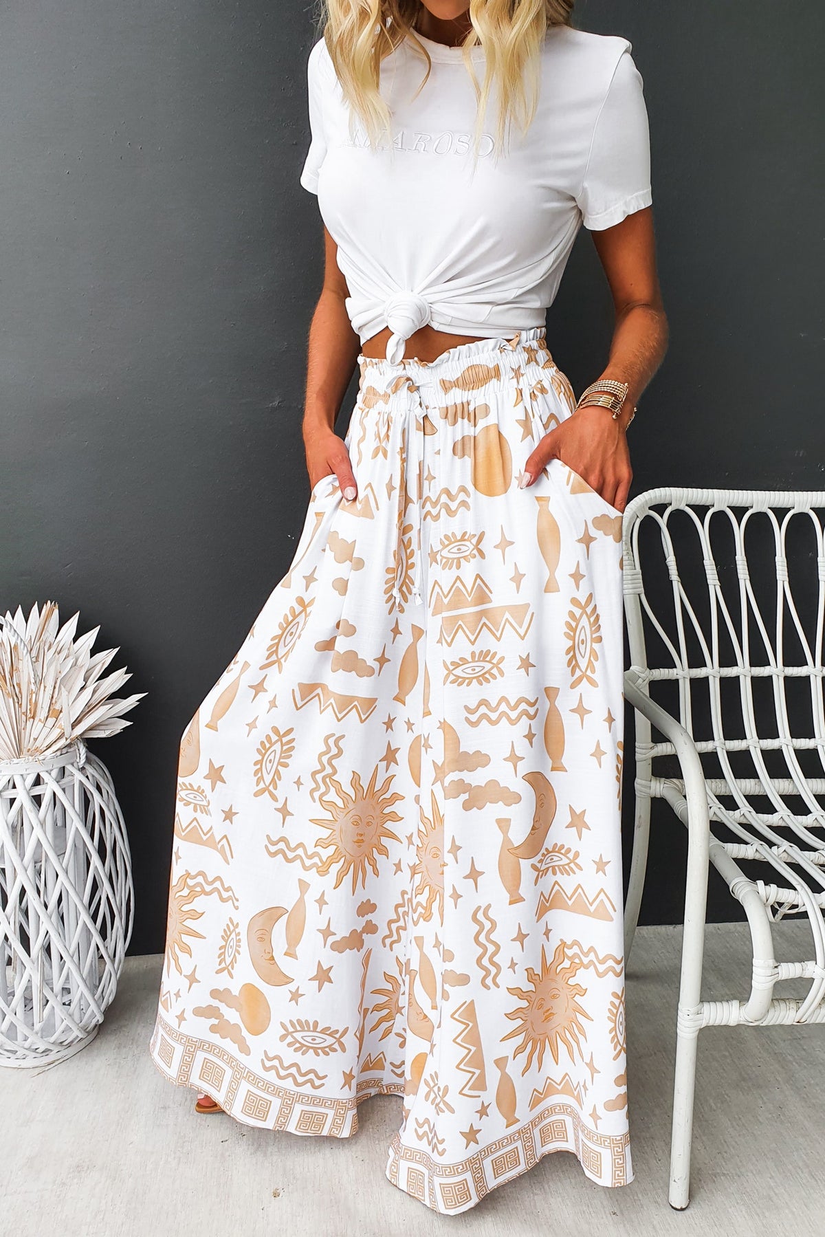 Woman wearing Amadi Pants, featuring abstract print, elastic waistband, and wide legs, styled with a knotted white top.