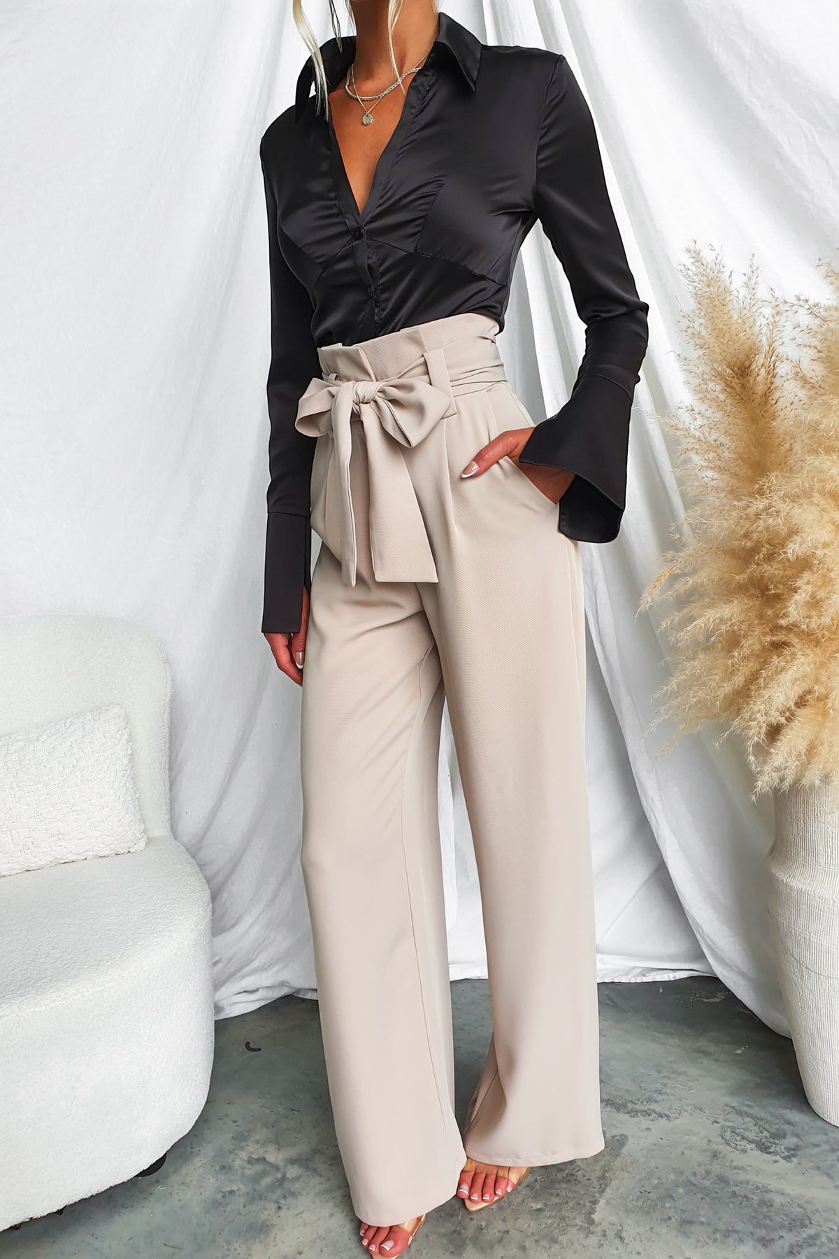 Model wearing beige Jaspin Pants with paper bag waist and fabric tie, paired with a black shirt.