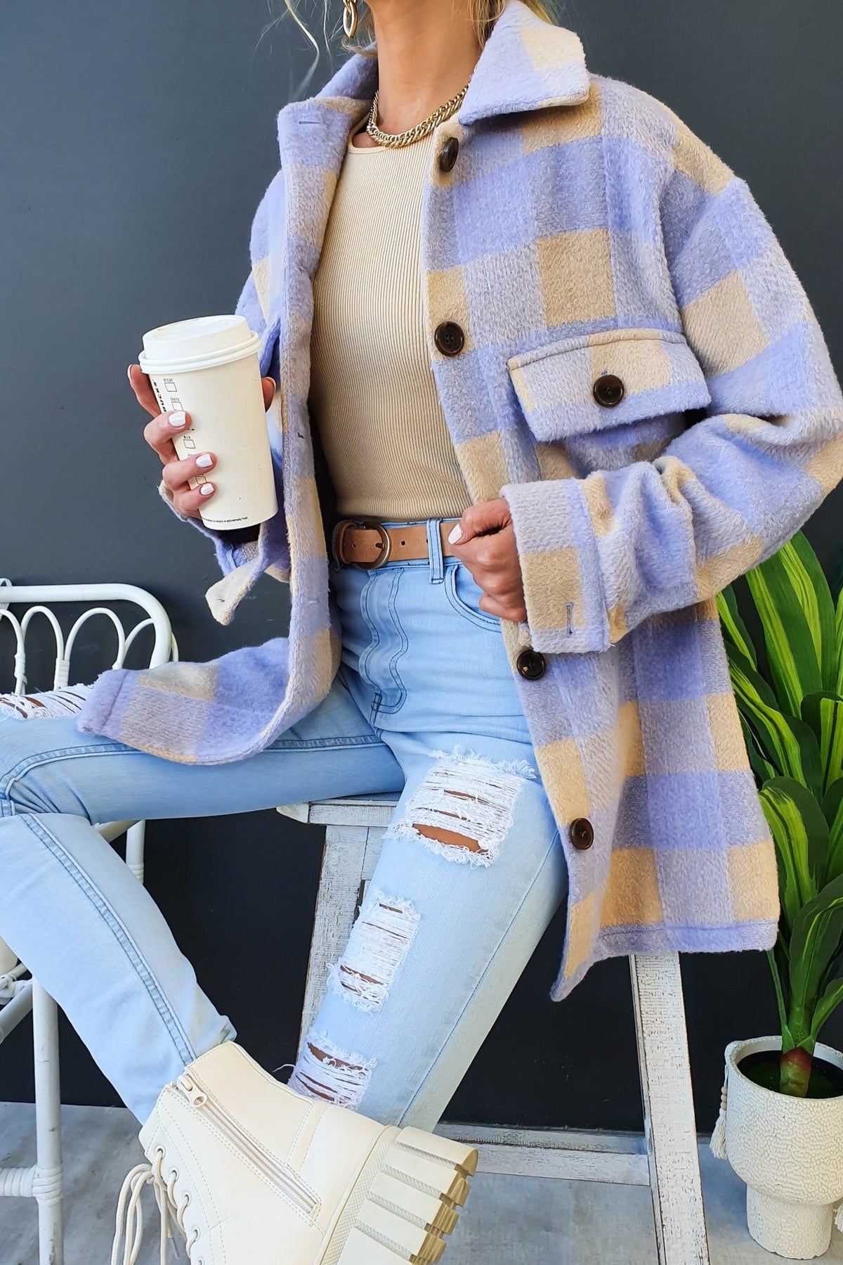 Stylish woman in a cozy blue and tan plaid shacket, holding a coffee cup, paired with ripped jeans and heeled boots.