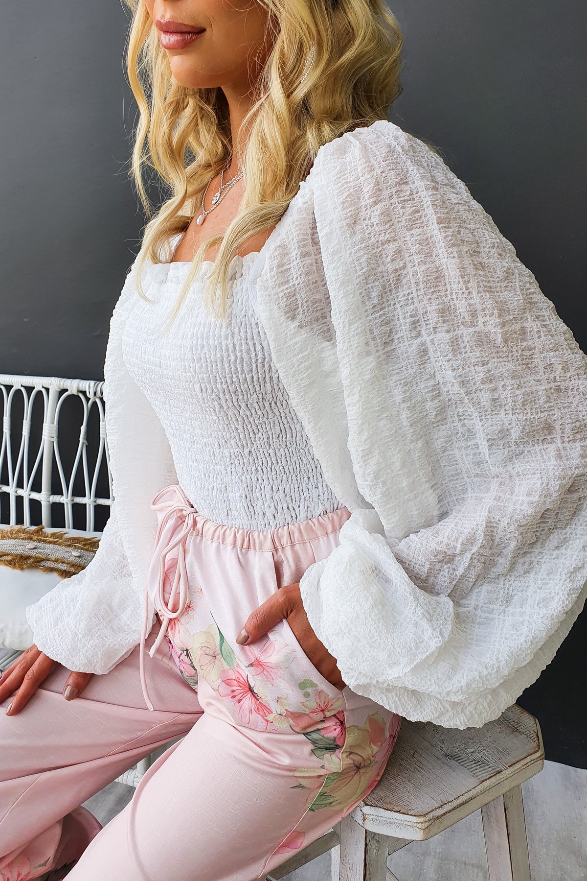 Model wearing Joey Top with square neckline and elastic sleeves, paired with floral pants, on a chair.