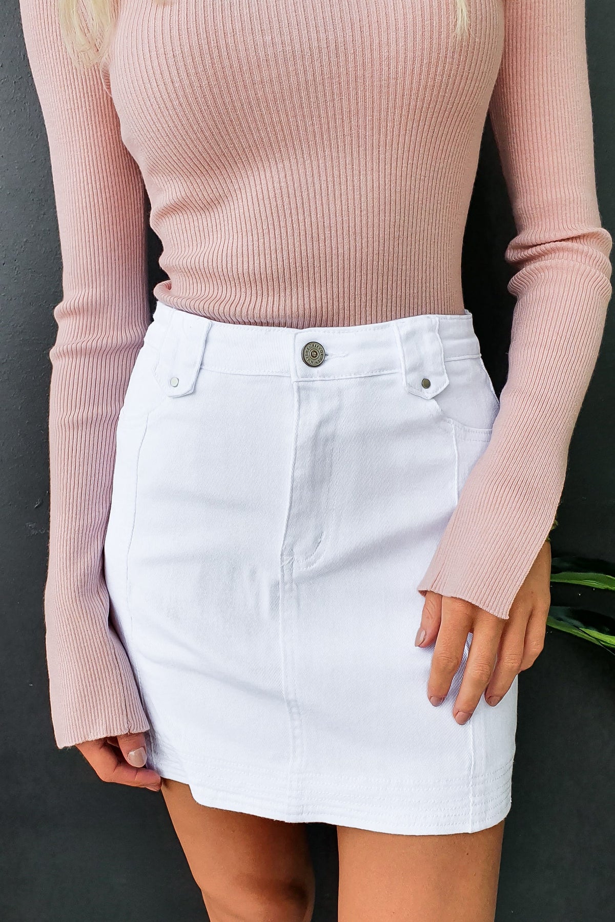 Model wearing a white denim skirt with a mid-high waist, paired with a pink ribbed sweater, showcasing casual style.