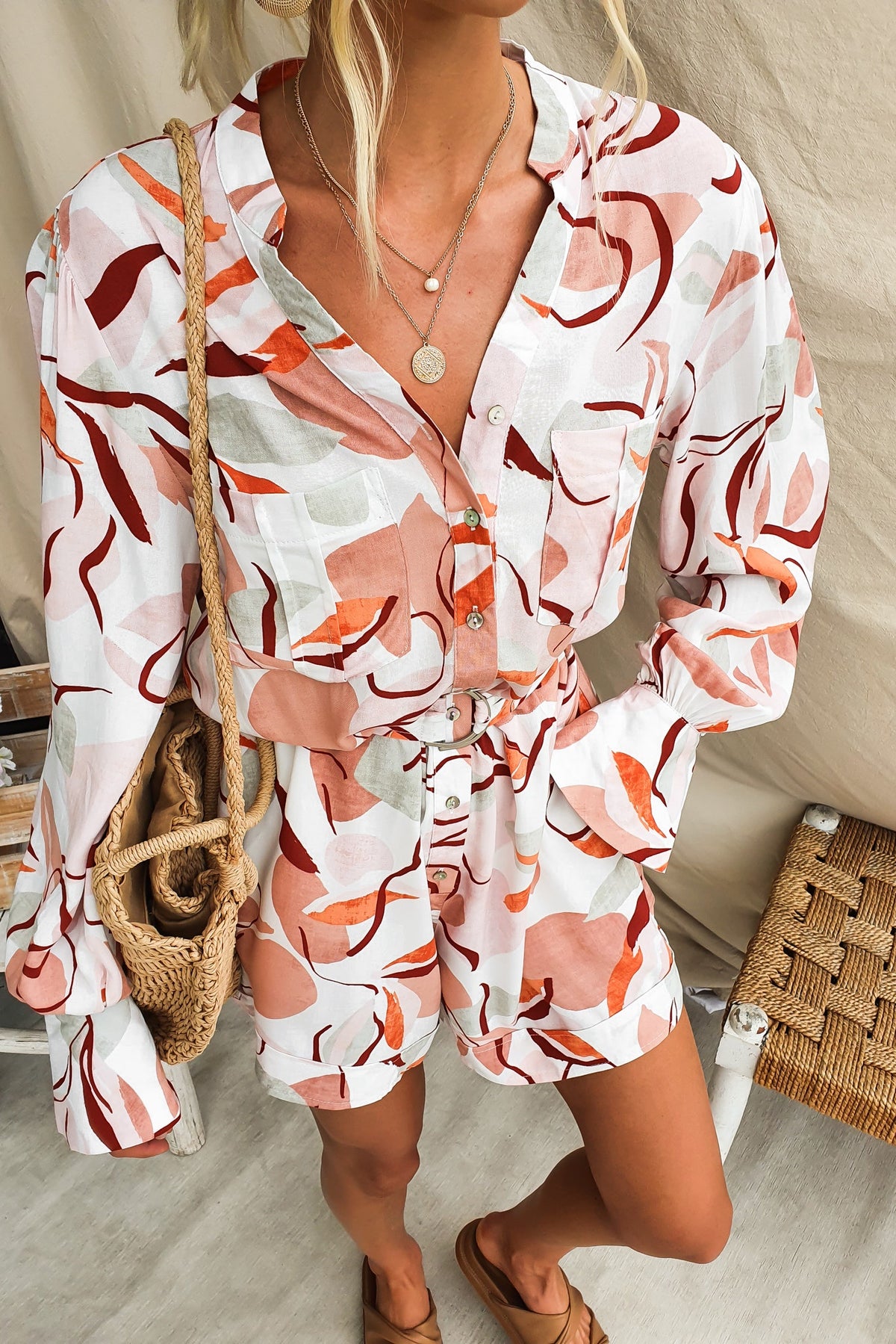 Model wearing Alfred Playsuit with abstract floral pattern and detachable belt, accessorized with a tote bag.