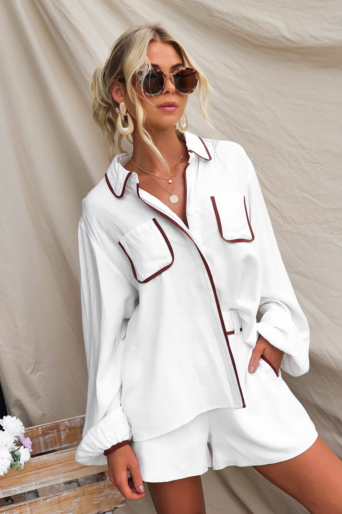 Woman in white Ronnie Shirt with pockets, sunglasses, and casual shorts; relaxed fit, stylish summer outfit.