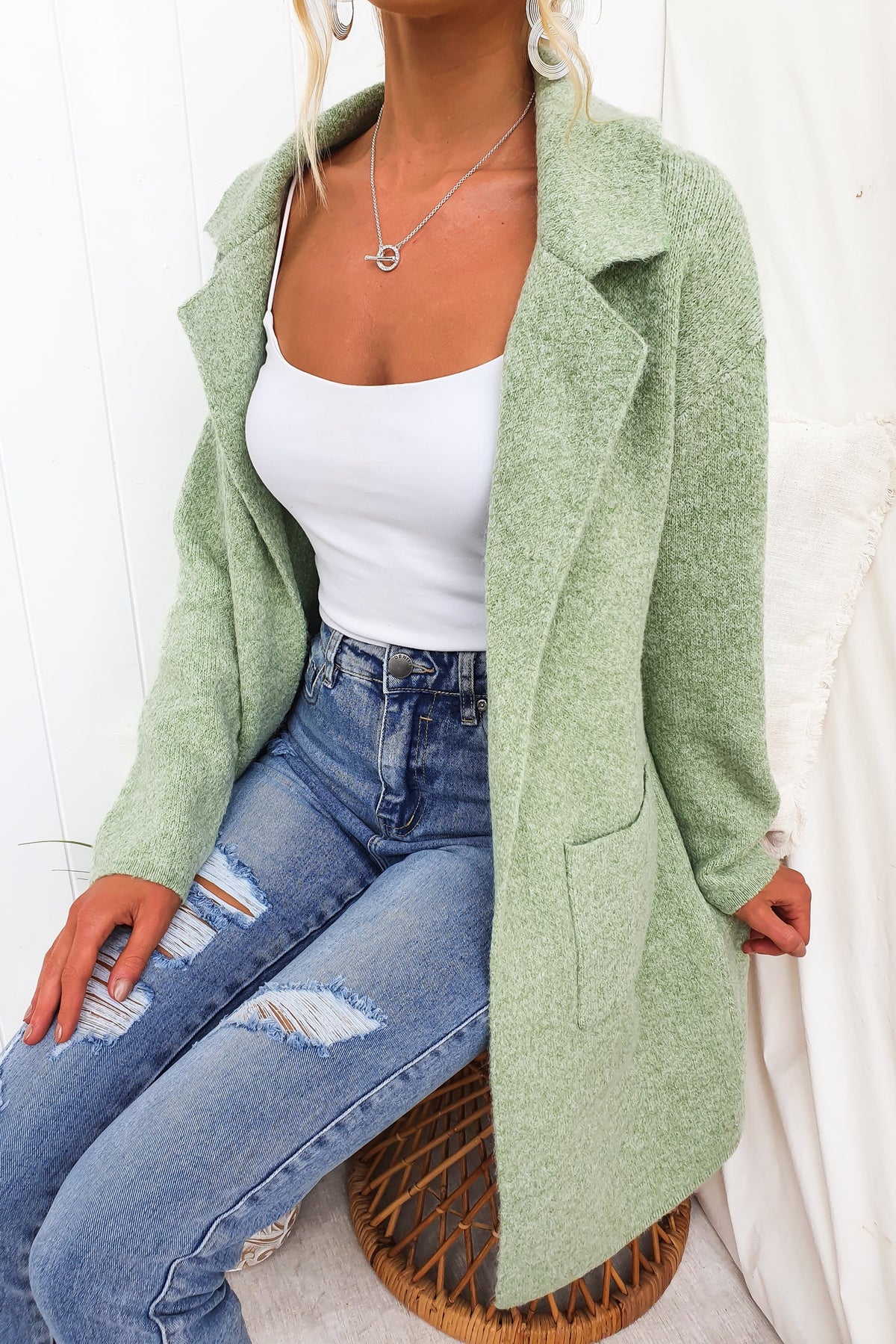 Sarlia Cardigan in soft green knit, featuring a collar and pockets, worn over a white tank top with distressed jeans.
