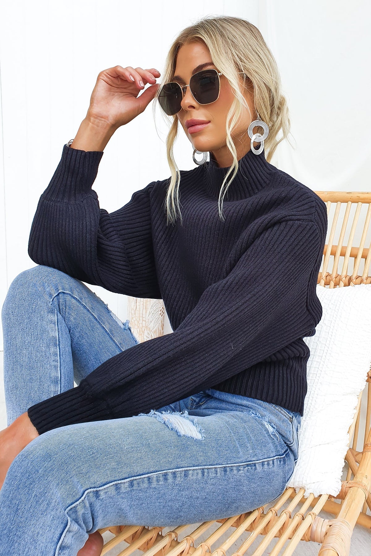 Model wearing Sola Jumper, a black ribbed knit mock neckline sweater, paired with sunglasses and jeans.