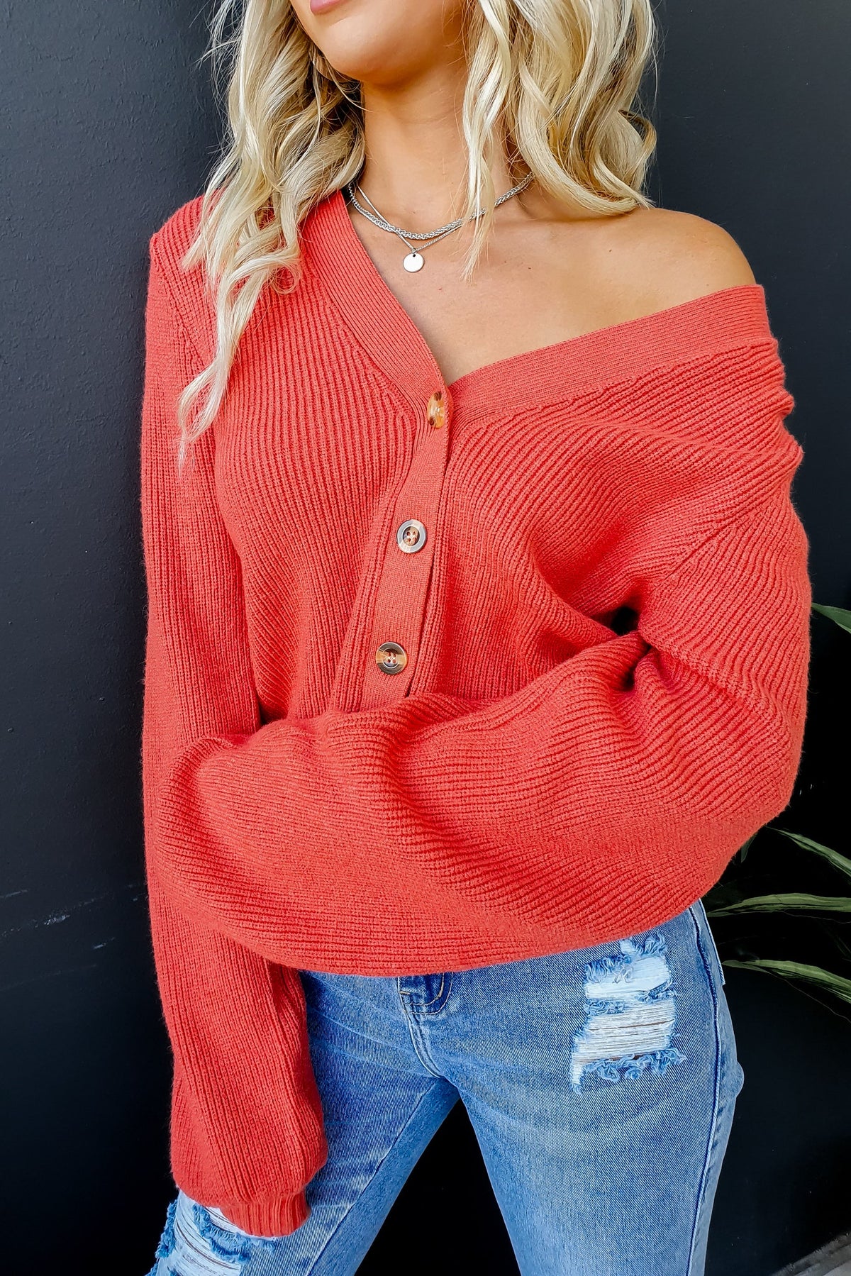 Modalla Cardigan in coral with V-neckline, button-up front, and ribbed knit material, worn with distressed jeans.