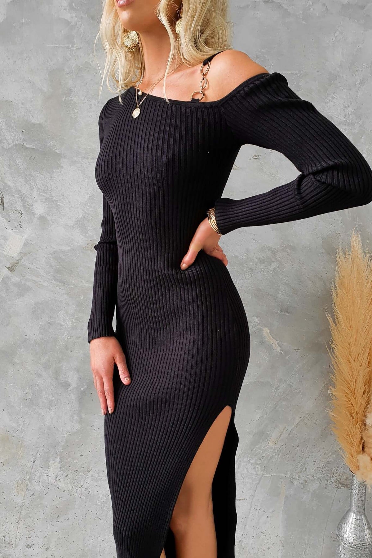 Black ribbed midi dress with asymmetric neckline and gold hardware detail, featuring a side split.