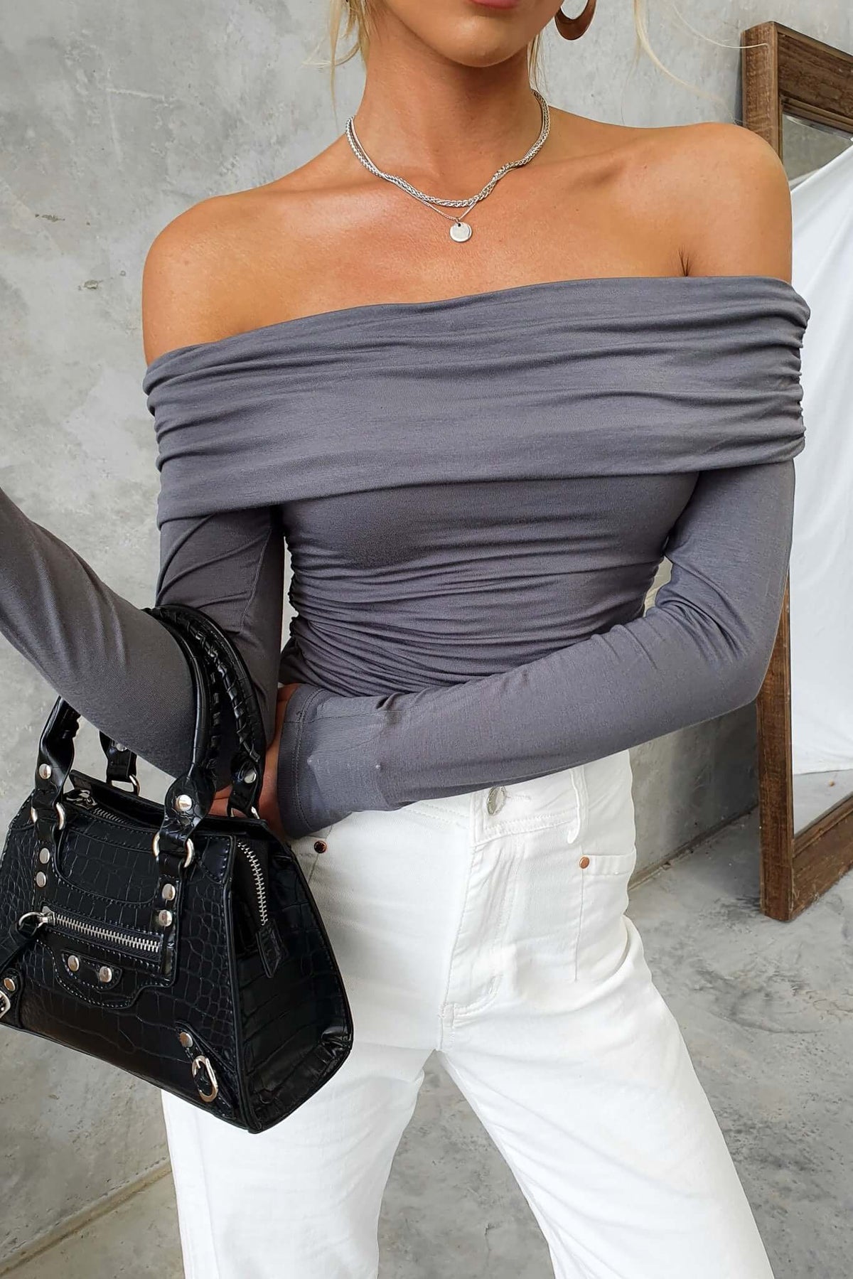 Woman wearing Harrie Top with off-shoulder neckline and ruched design, paired with a black handbag.