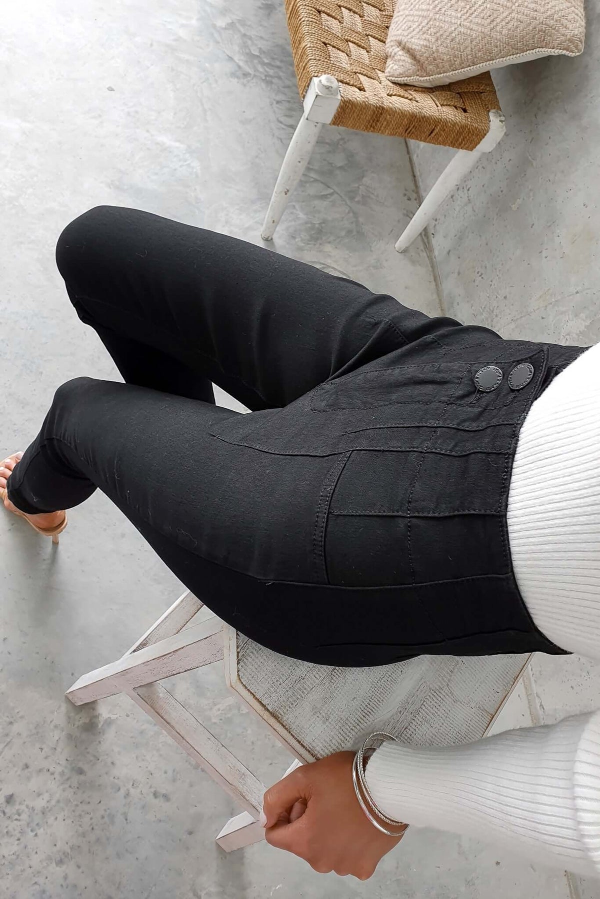 Okara Jeans in black denim with mid-high waist and two-button closure, styled by a seated model.