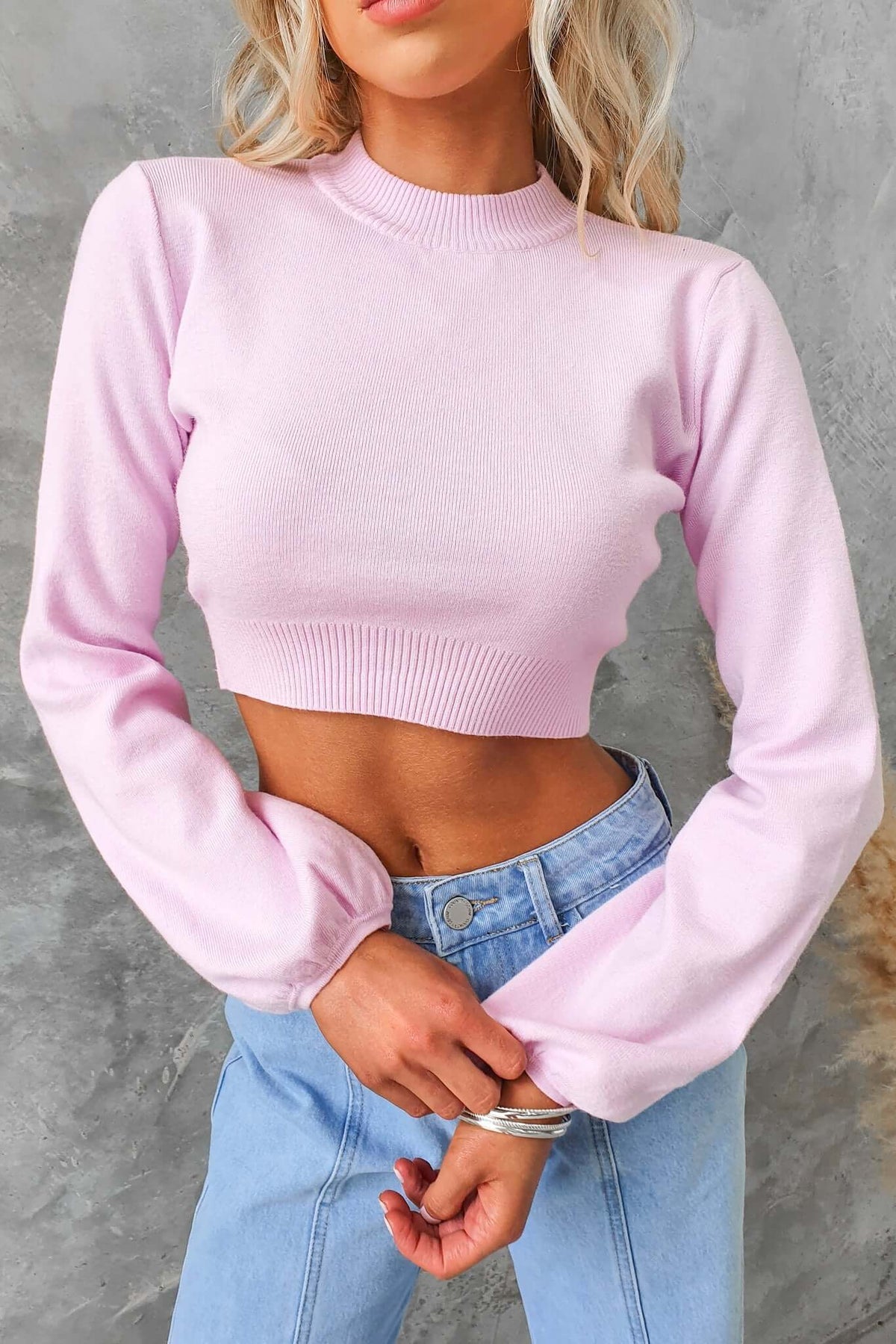 Sora Jumper in light pink, featuring high neckline and balloon sleeves, paired with light blue jeans.