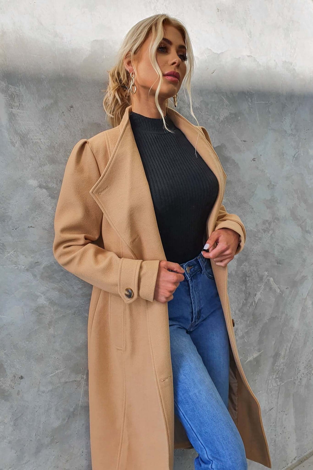 Stylish longline Ortona coat in camel color, paired with a fitted black top and blue jeans, showcasing modern fashion.