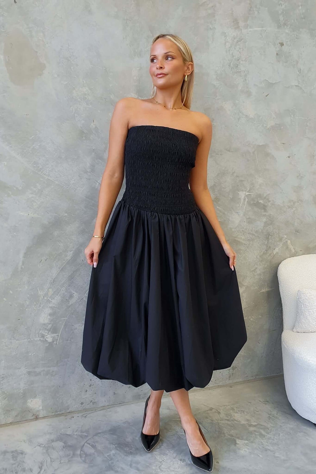 Model wearing a black strapless Cadro Midi Dress with an elastic bodice and full skirt against a minimalist backdrop.