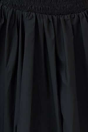 Close-up of a black midi dress fabric with gathered elastic bodice, featuring soft pleats and a sleek texture.