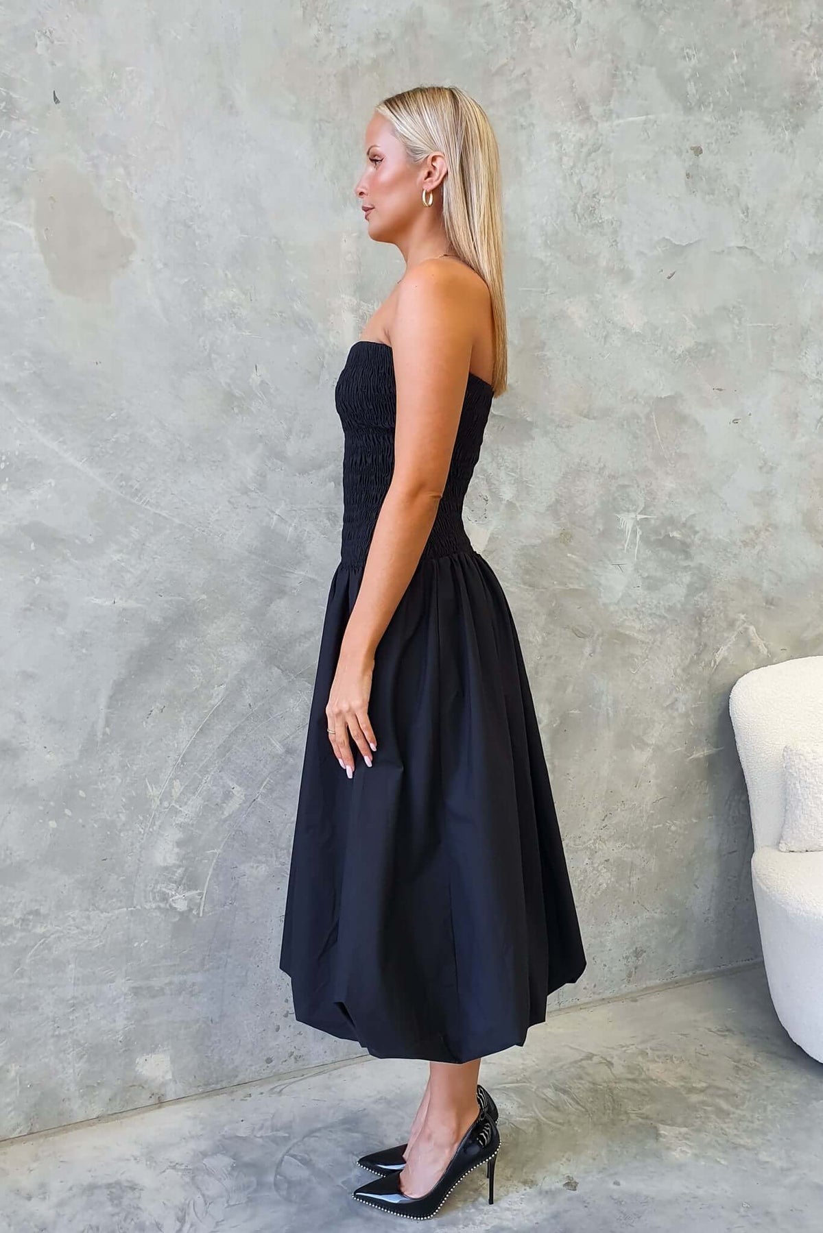 Side view of a woman wearing a black strapless midi dress with an elastic bodice and flared skirt.