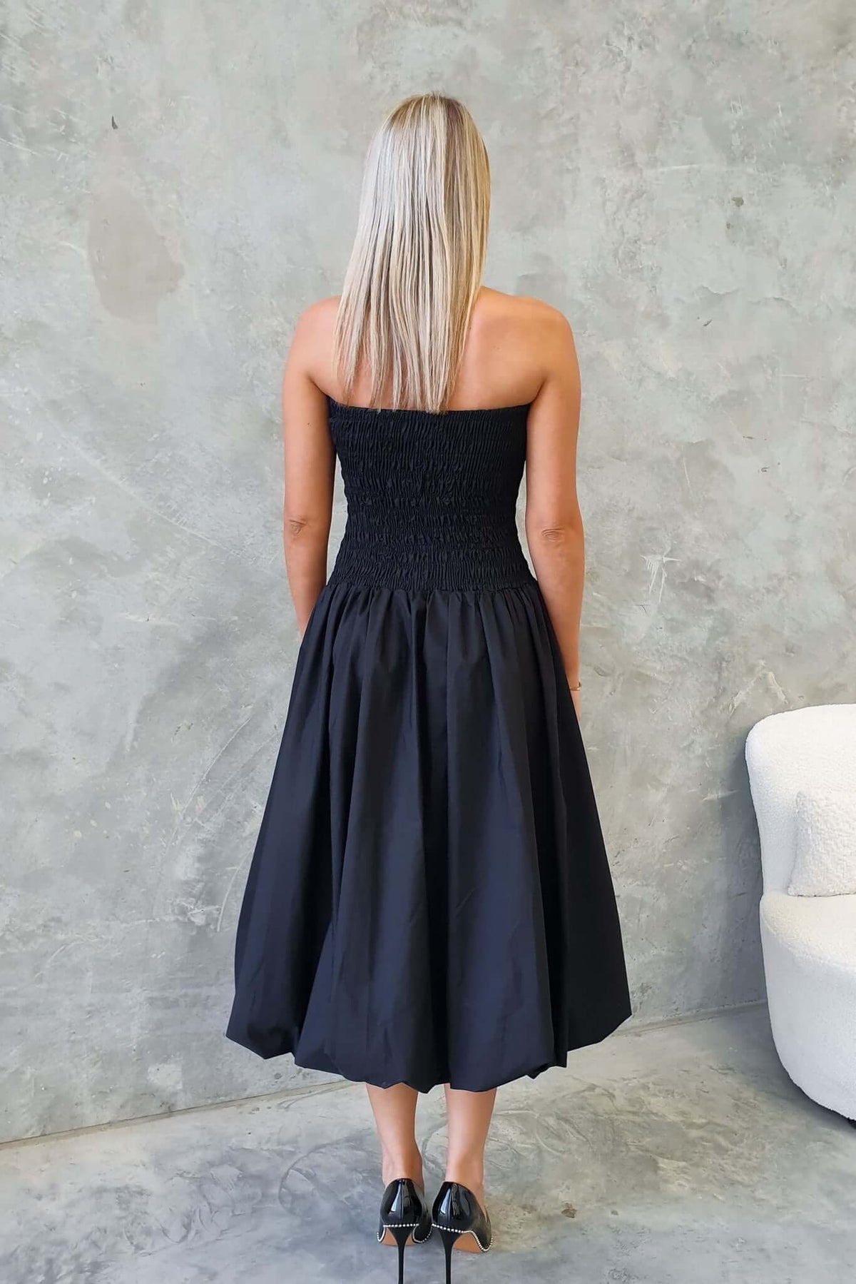 Back view of a strapless black midi dress with a smocked bodice, showcasing its elegant design and flowy skirt.