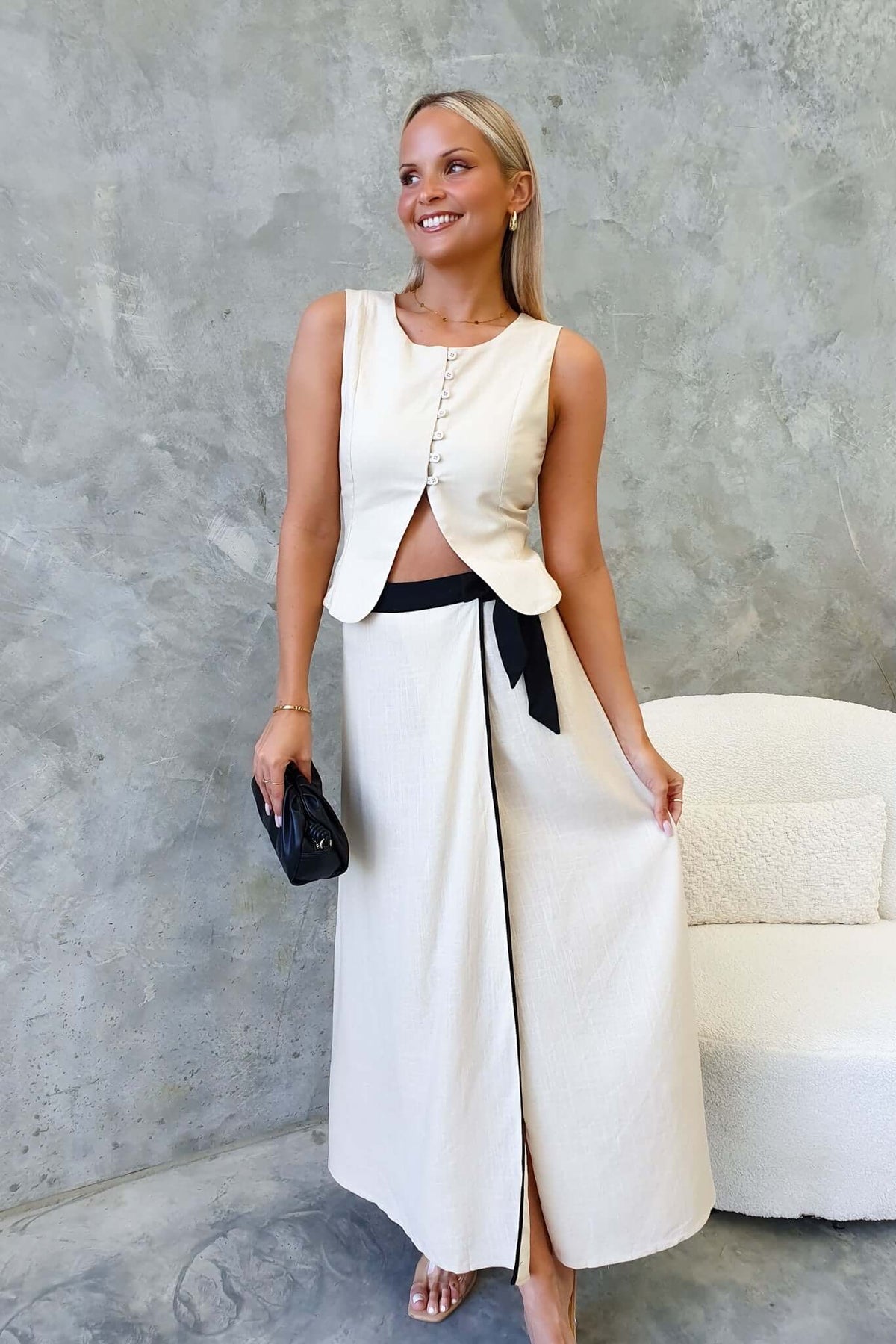 Model wearing a chic linen look Tuscan top and maxi skirt, styled with a black accessory against a textured background.