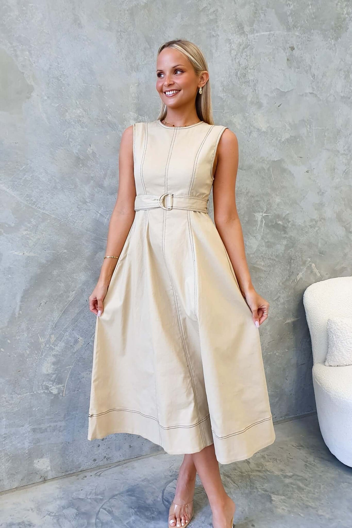 Woman wearing a beige denim midi dress with a belt, styled against a minimalist backdrop.