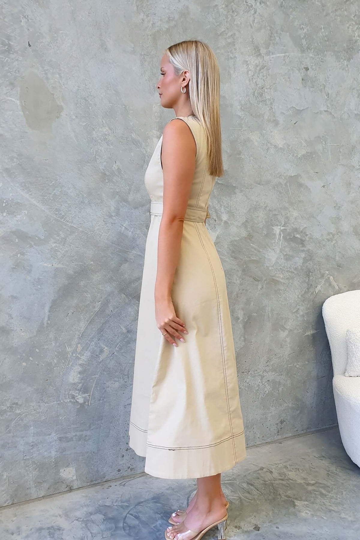 Side view of a model wearing a beige denim midi dress, featuring a fitted silhouette and elegant design.