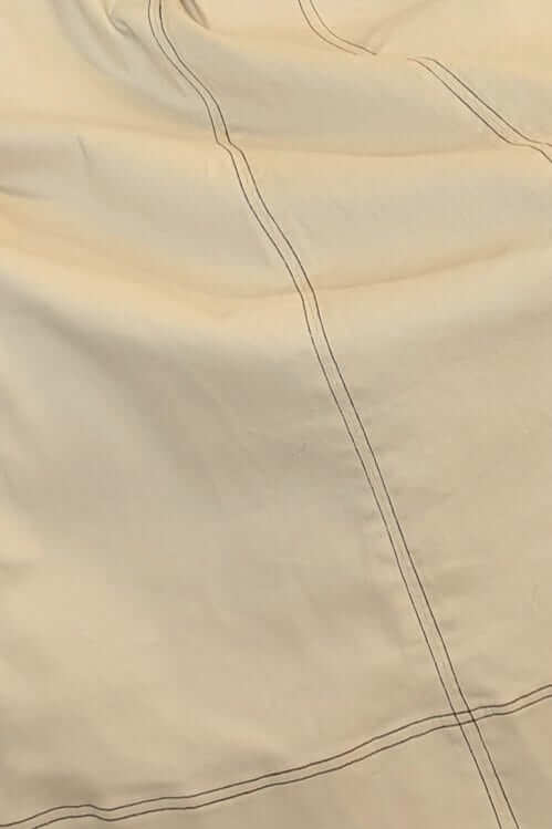 Close-up of light beige fabric with stitching, showcasing texture and detail of a stylish garment.