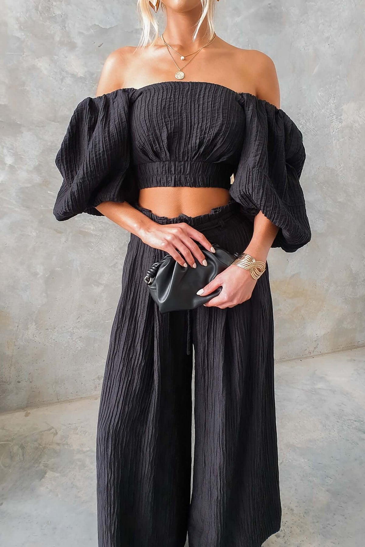 Model wearing a black Know Better top with square neckline and balloon sleeves, paired with black pants and accessories.