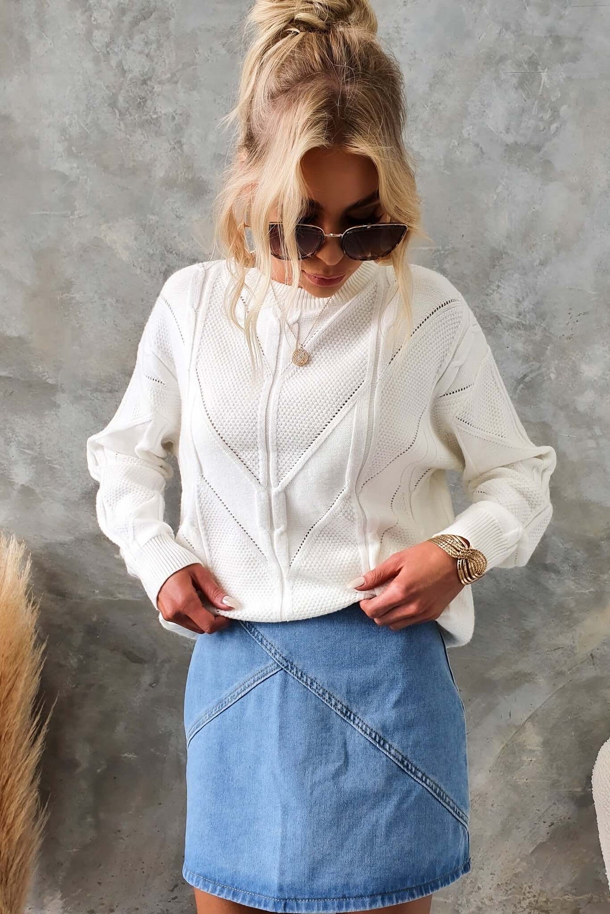 Model wearing white Becker Jumper with round neckline and cable knit, paired with denim skirt, showcasing relaxed fashion style.