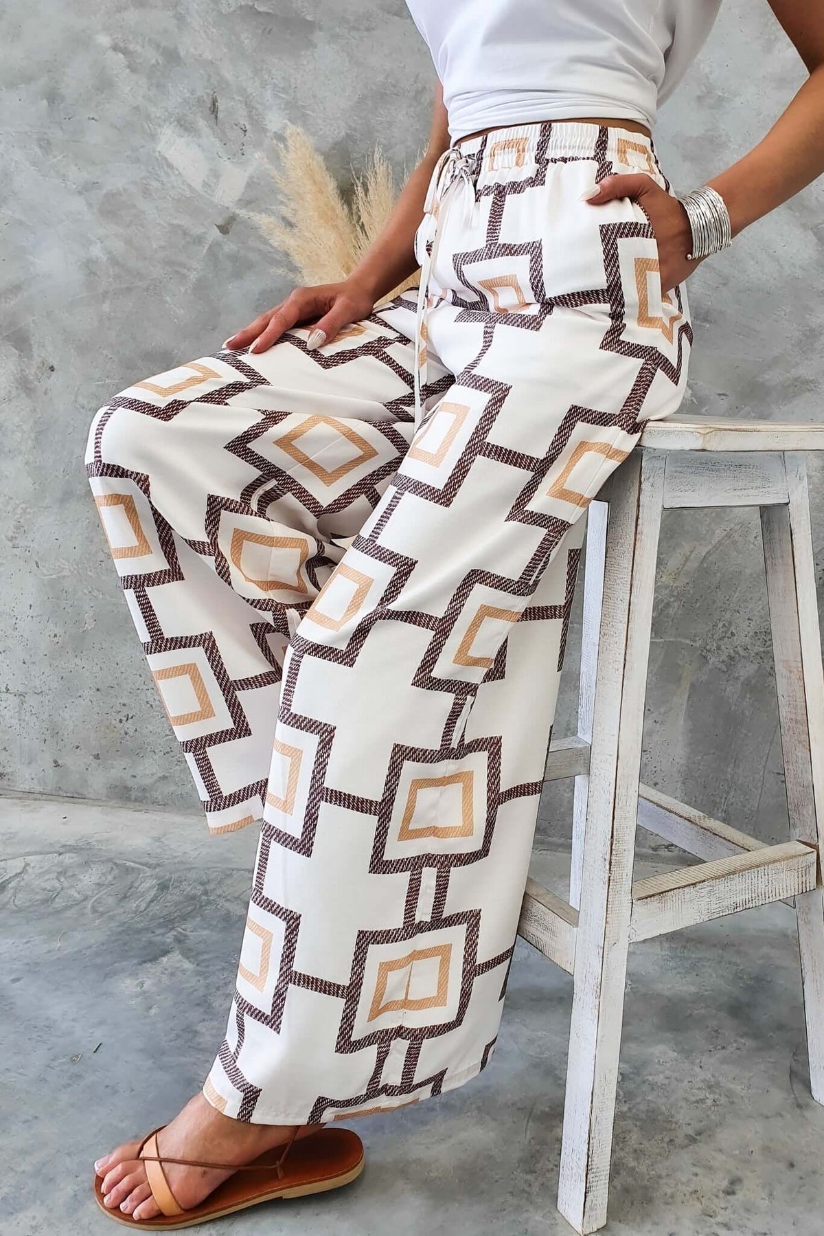 Aiden Pants with geometric pattern, high-waisted fit, and lined pockets, styled with a white top and sandals.