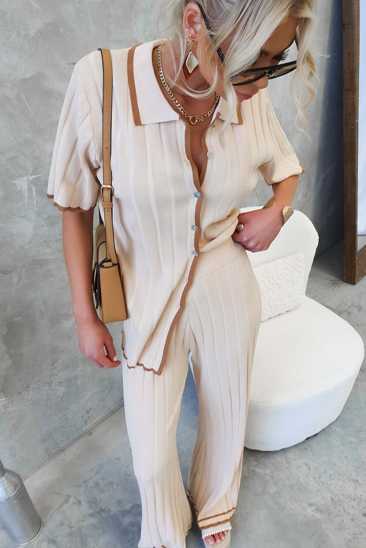 Woman wearing Jodie Shirt in ribbed knit, light beige color, button-up style, paired with matching pants and accessories.