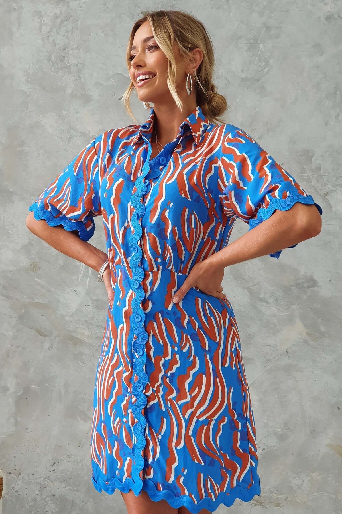 Model wearing Alfonzo Dress featuring a vibrant blue and orange design, button-up front, and scalloped sleeves.