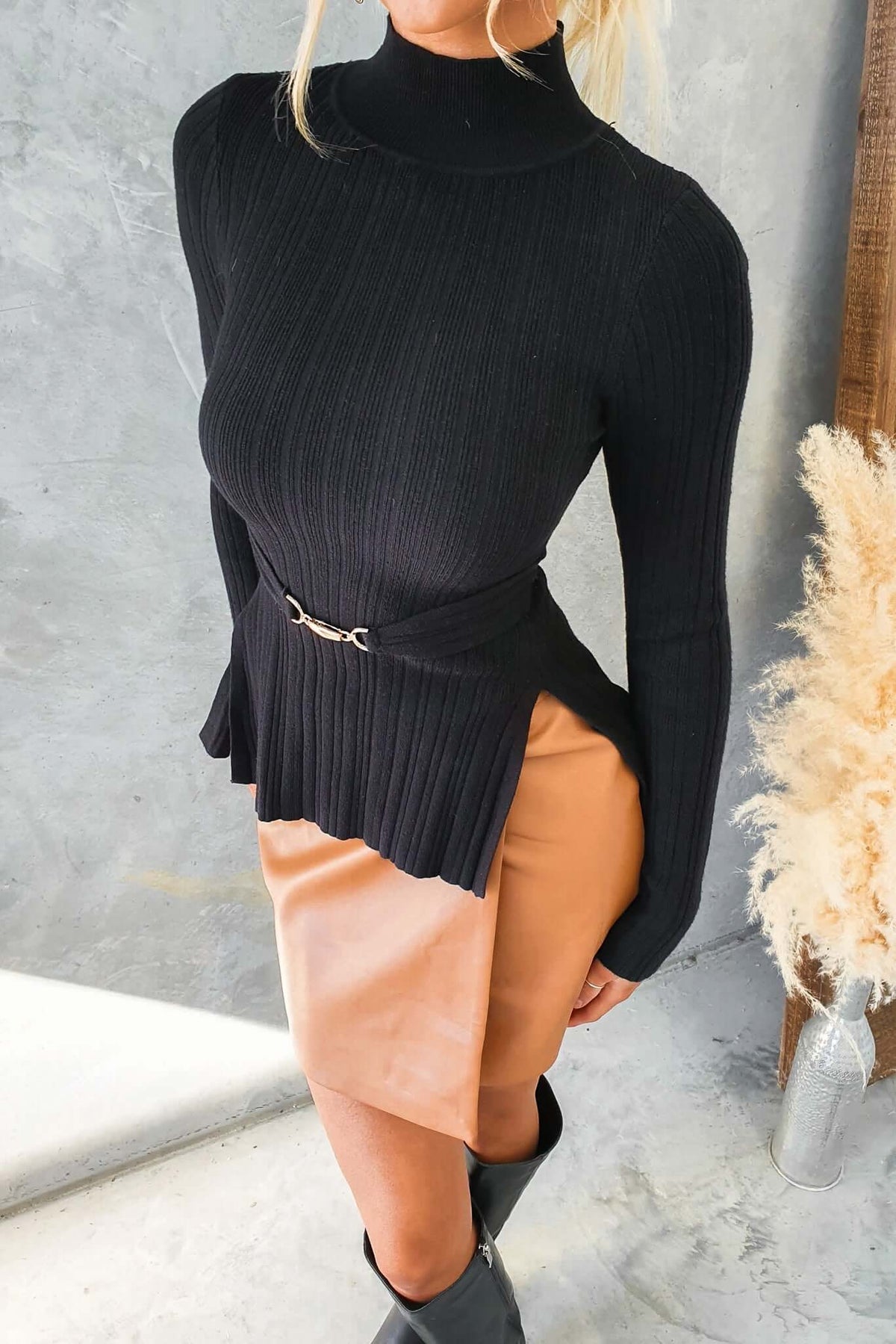 Ollie Top in black with high neckline and buckle detail, styled with a tan skirt, showcasing ribbed knit material and stretch fit.