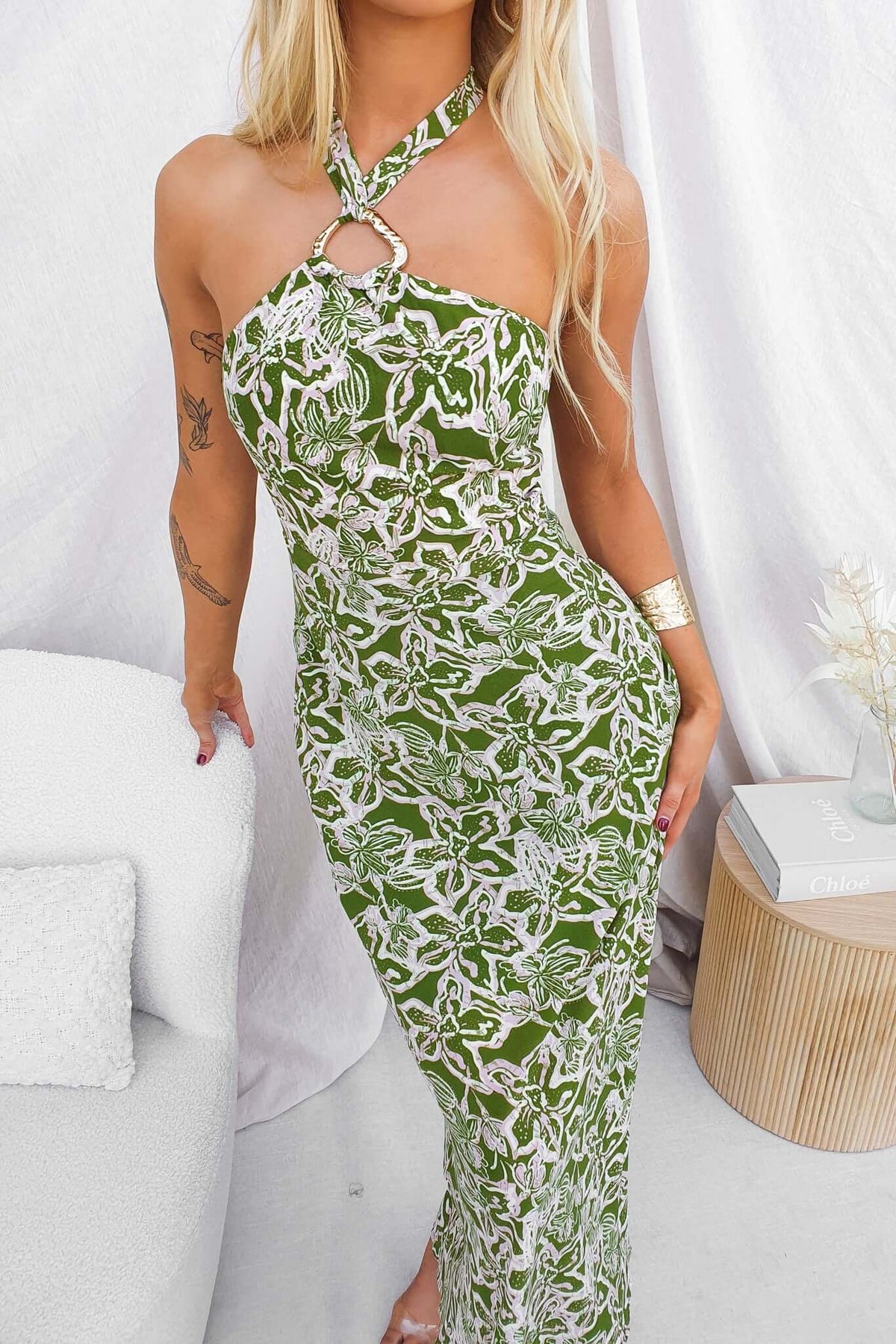 Model showcasing Nino Maxi Dress in green floral print with adjustable tie neckline and gold hardware detail.