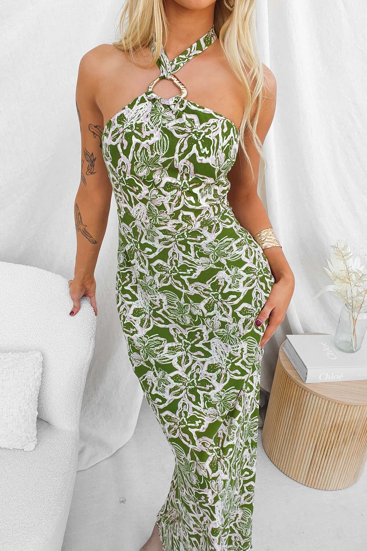 Nino Maxi Dress featuring an adjustable tie neckline, gold hardware, and floral design against a green background.