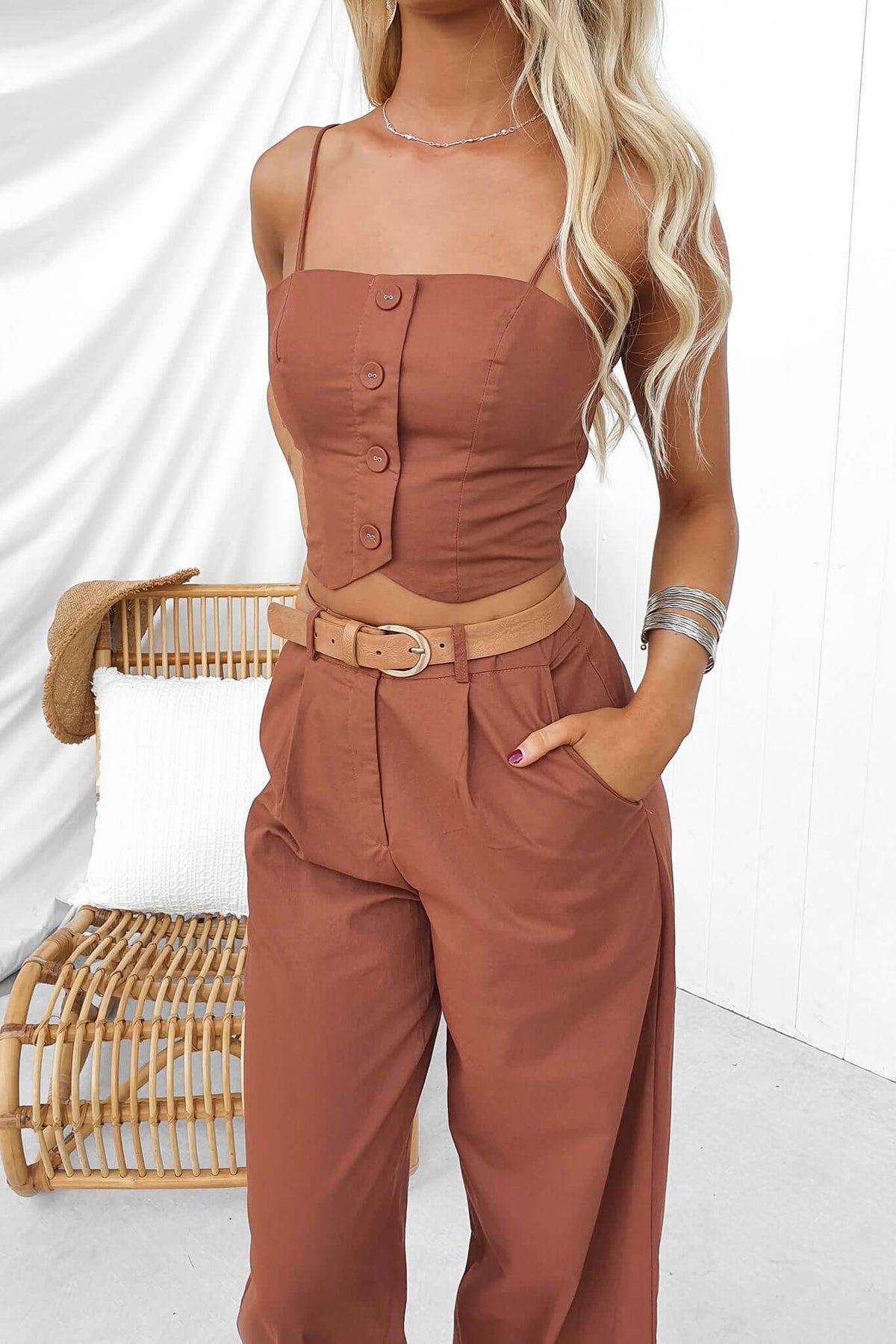 Woman wearing Downtown Top with adjustable spaghetti straps and buttons, styled with high-waisted beige pants.