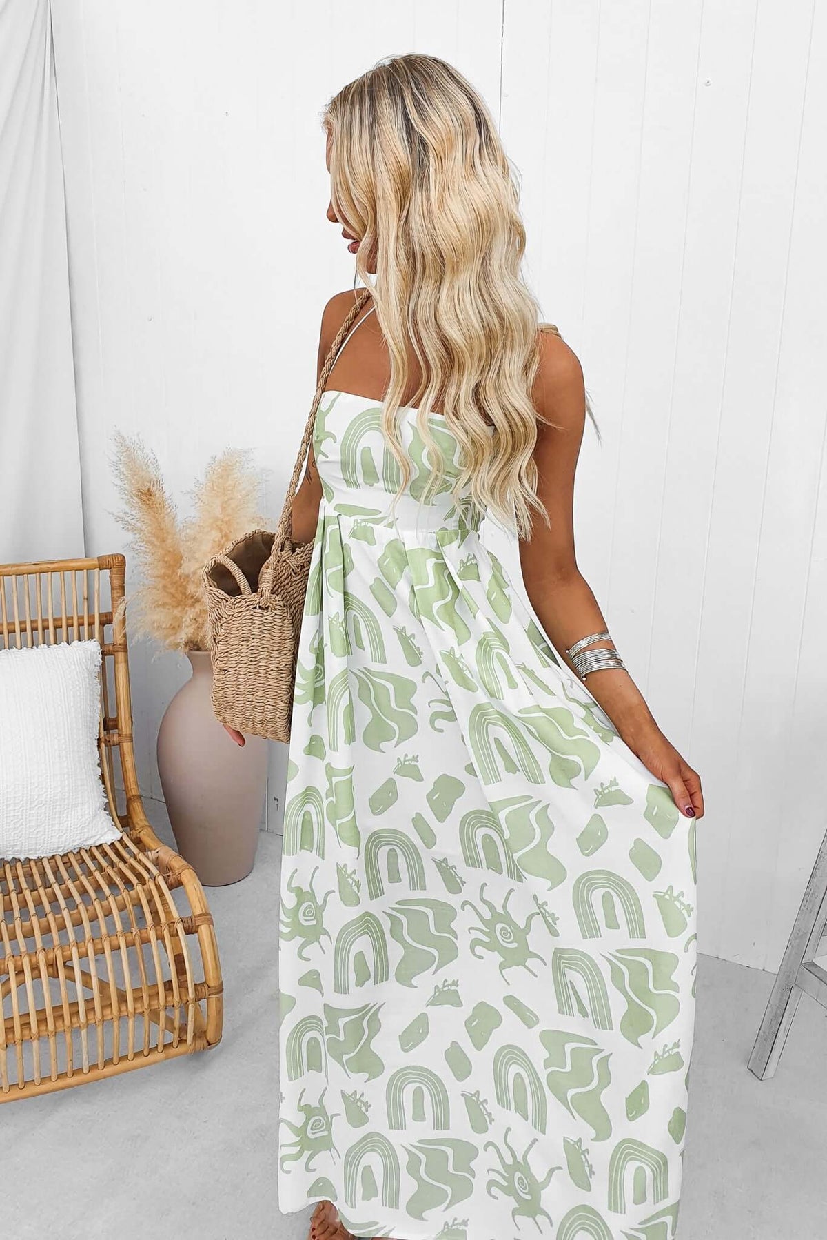 Woman wearing Derry Maxi Dress with adjustable straps, square neckline, in green and white print, standing in a bright space.