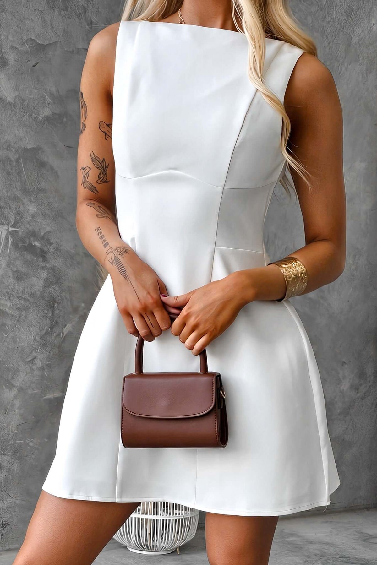 Model in a chic white scoop back dress, holding a brown handbag, showcasing a stylish and elegant outfit.