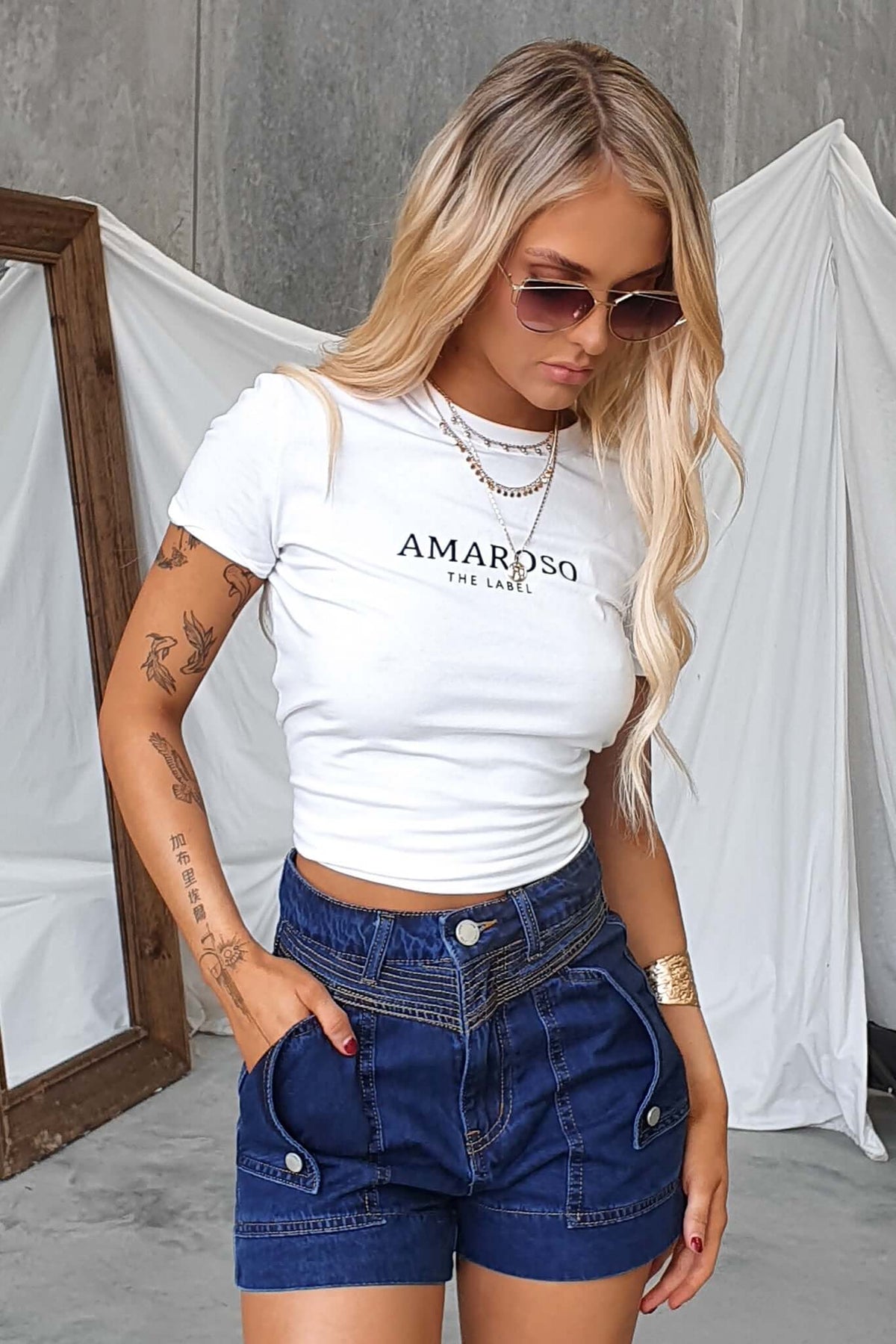 Model wearing AMAROSO tee and Kodiak shorts, featuring a casual style with button pockets and a trendy fit.