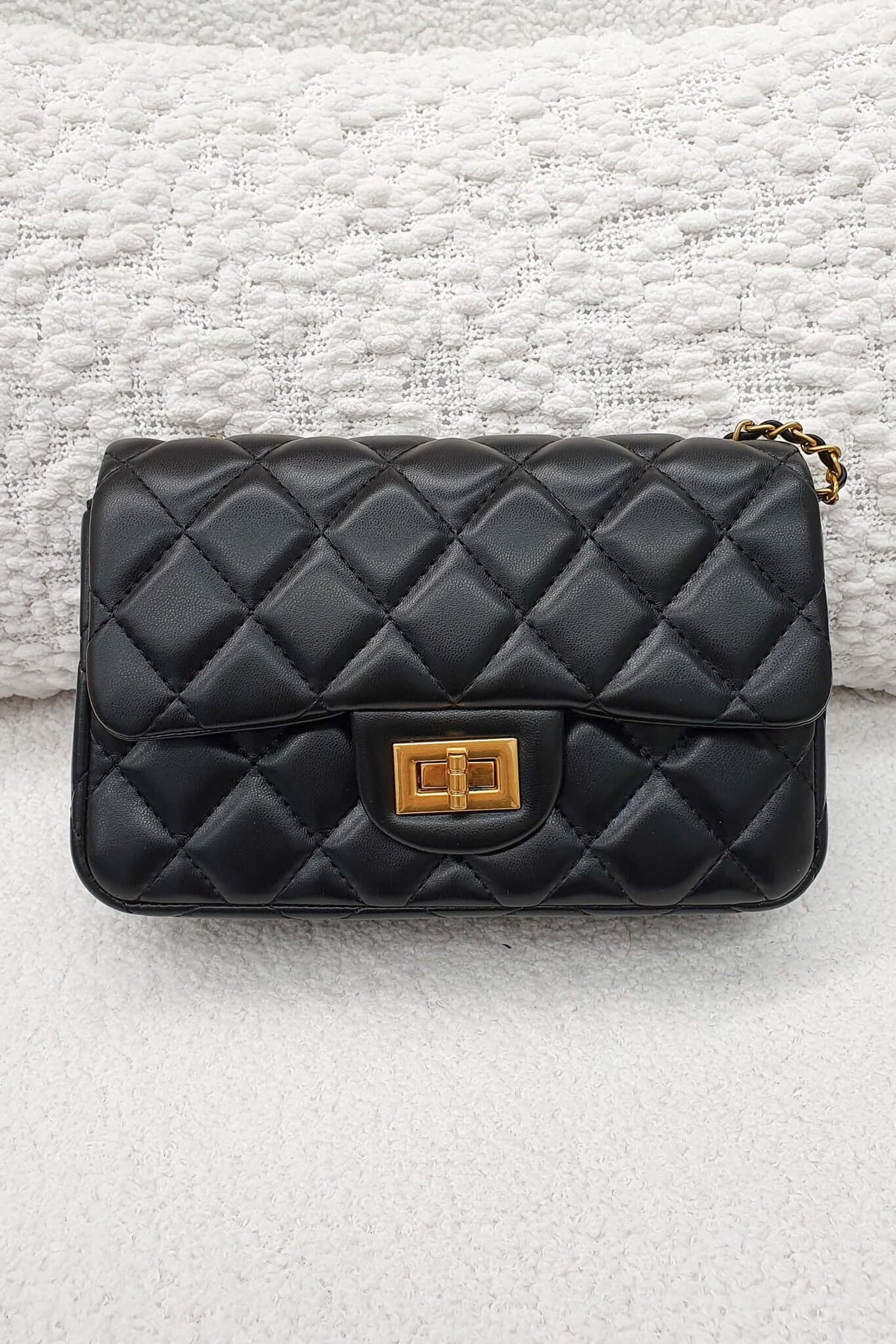 Chic black Chelsea Bag with quilted finish and gold hardware on textured background.