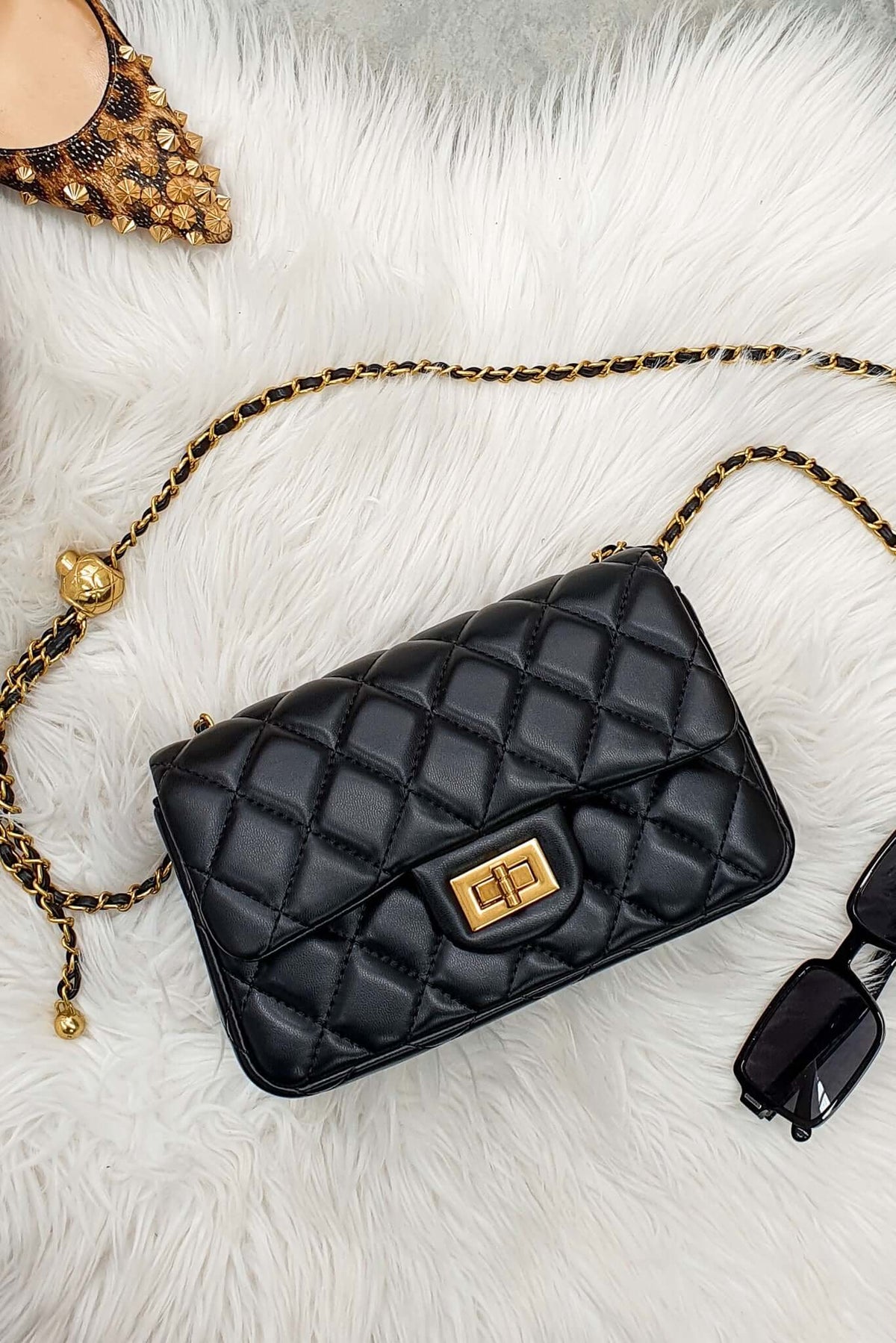 Chic black Chelsea bag with quilted finish, gold hardware, and stylish strap on a plush background.