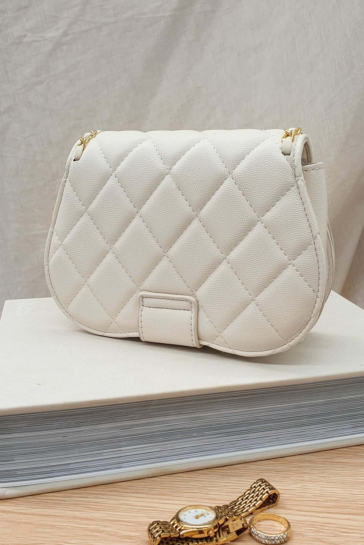 White quilted Vera Bag resting on a stack of books, showcasing its chic, vegan leather design.