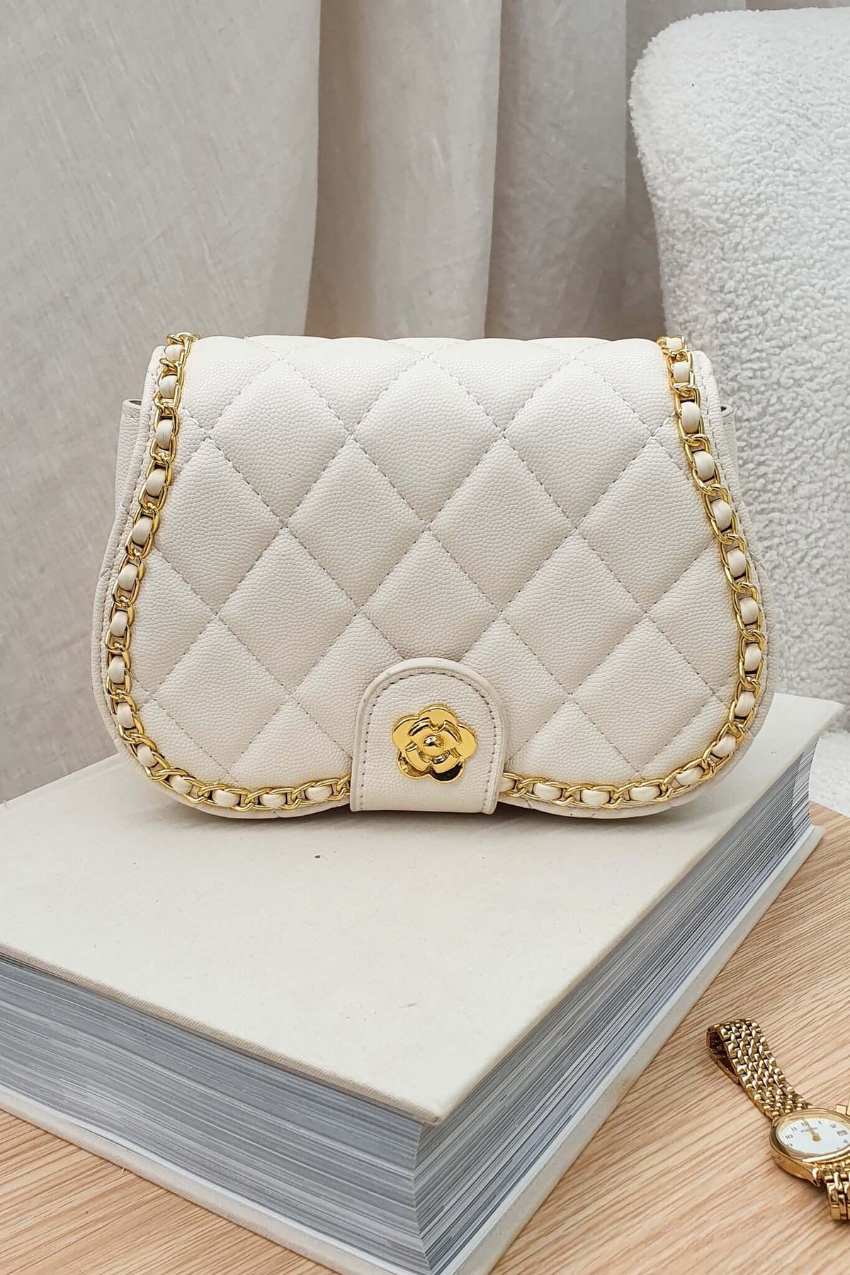 Chic Vera Bag in quilted white vegan leather with gold chain detail, elegantly placed on a stack of books.
