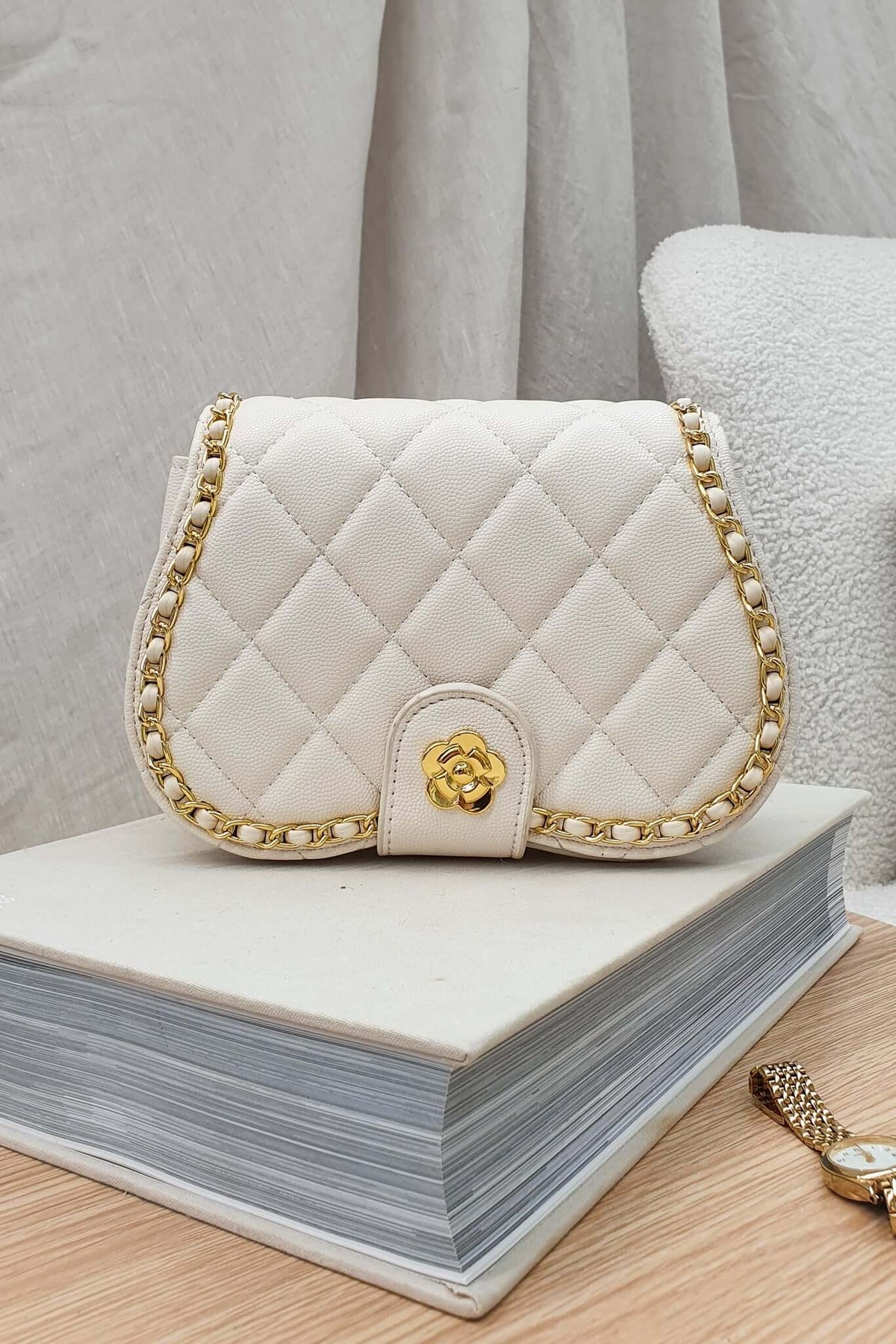 Elegant white quilted handbag with gold chain detailing, resting on a stack of books.