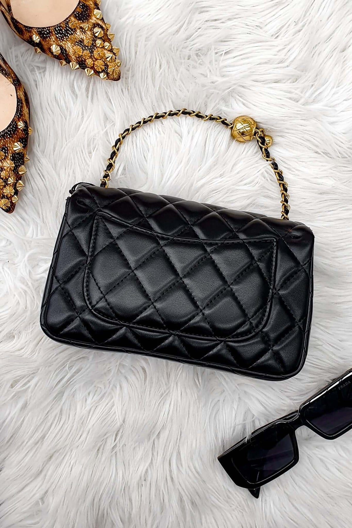 Chic Chelsea Bag in quilted black vegan leather with gold chain strap, styled with heels and sunglasses.