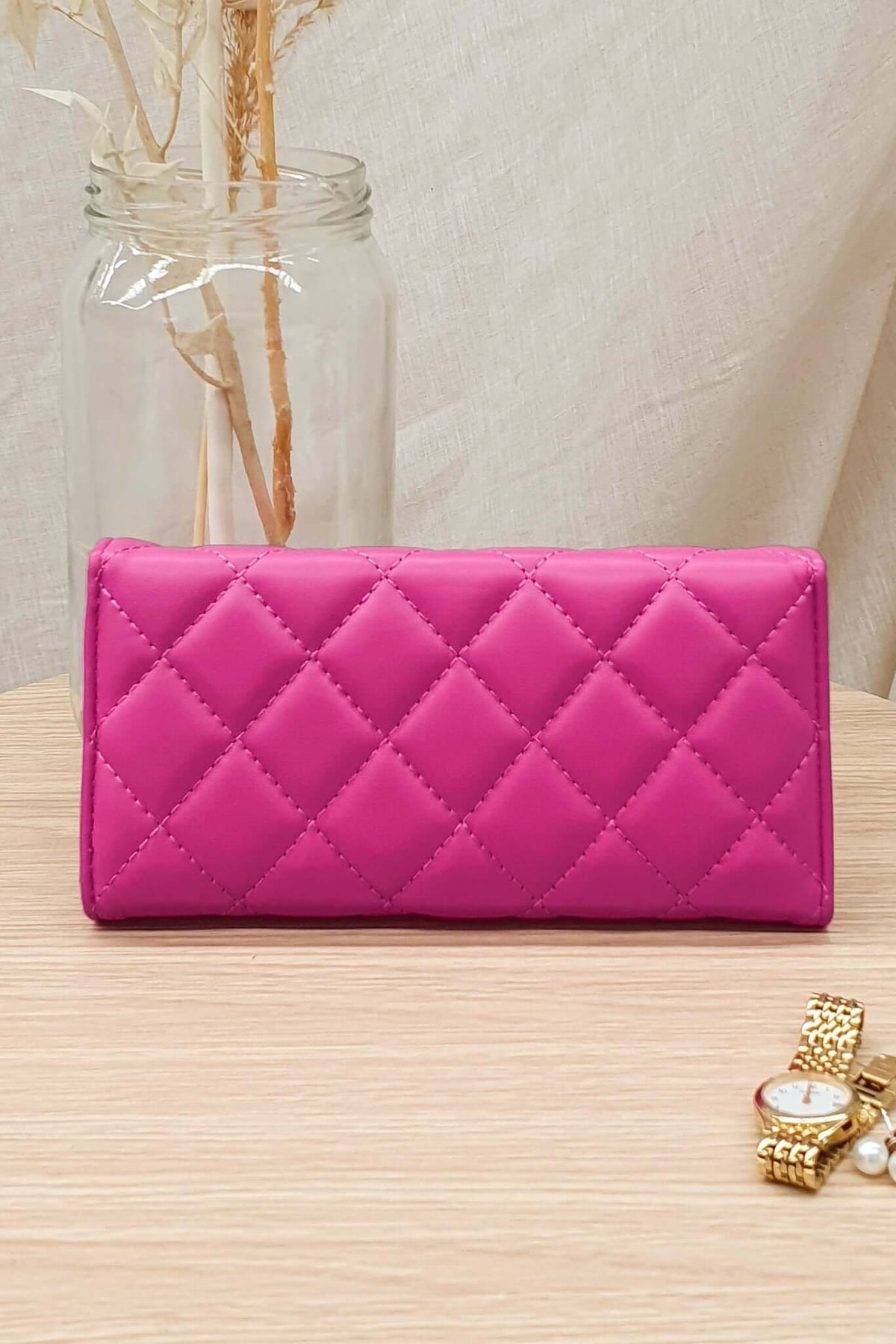 Asta Wallet in vibrant pink vegan leather, featuring a quilted design, displaying on a wooden table with minimalist decor.