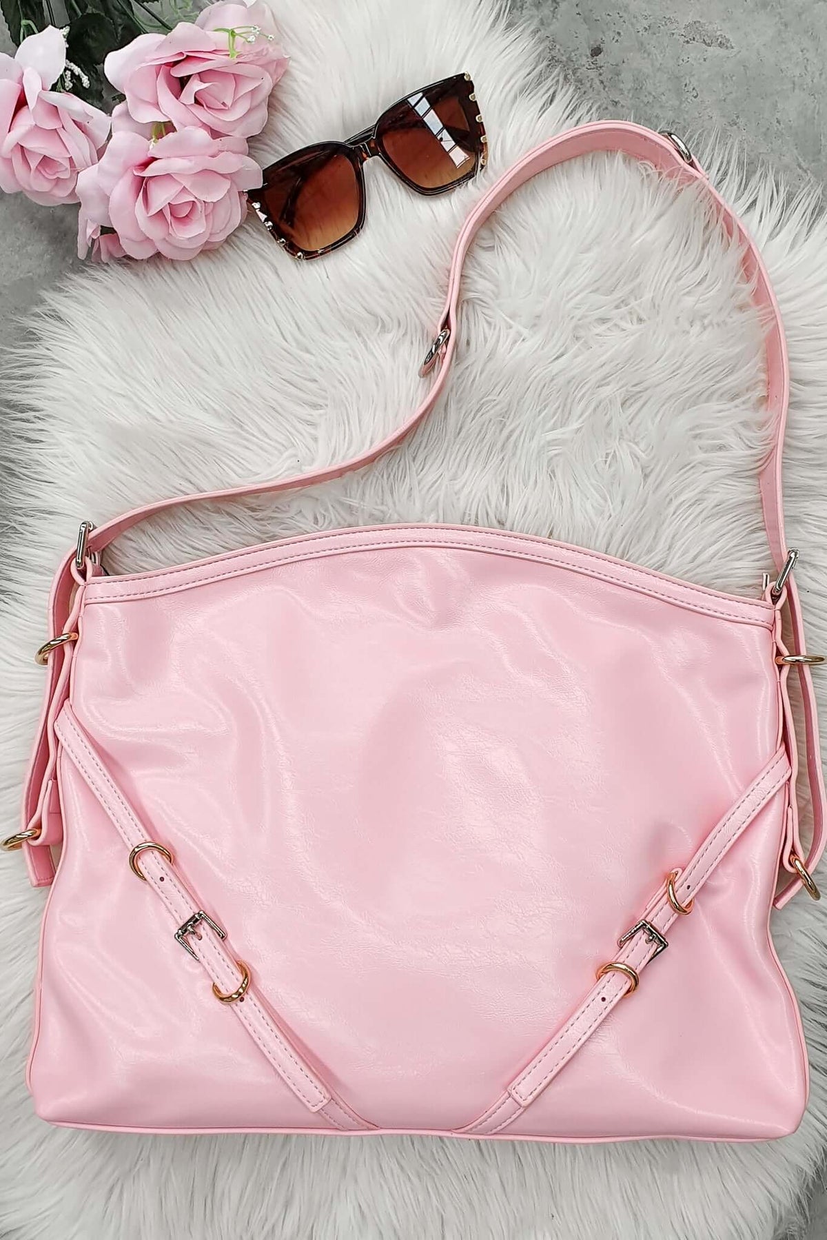 Bily Bag in pink resting on a fluffy white surface, paired with stylish sunglasses and pink flowers.